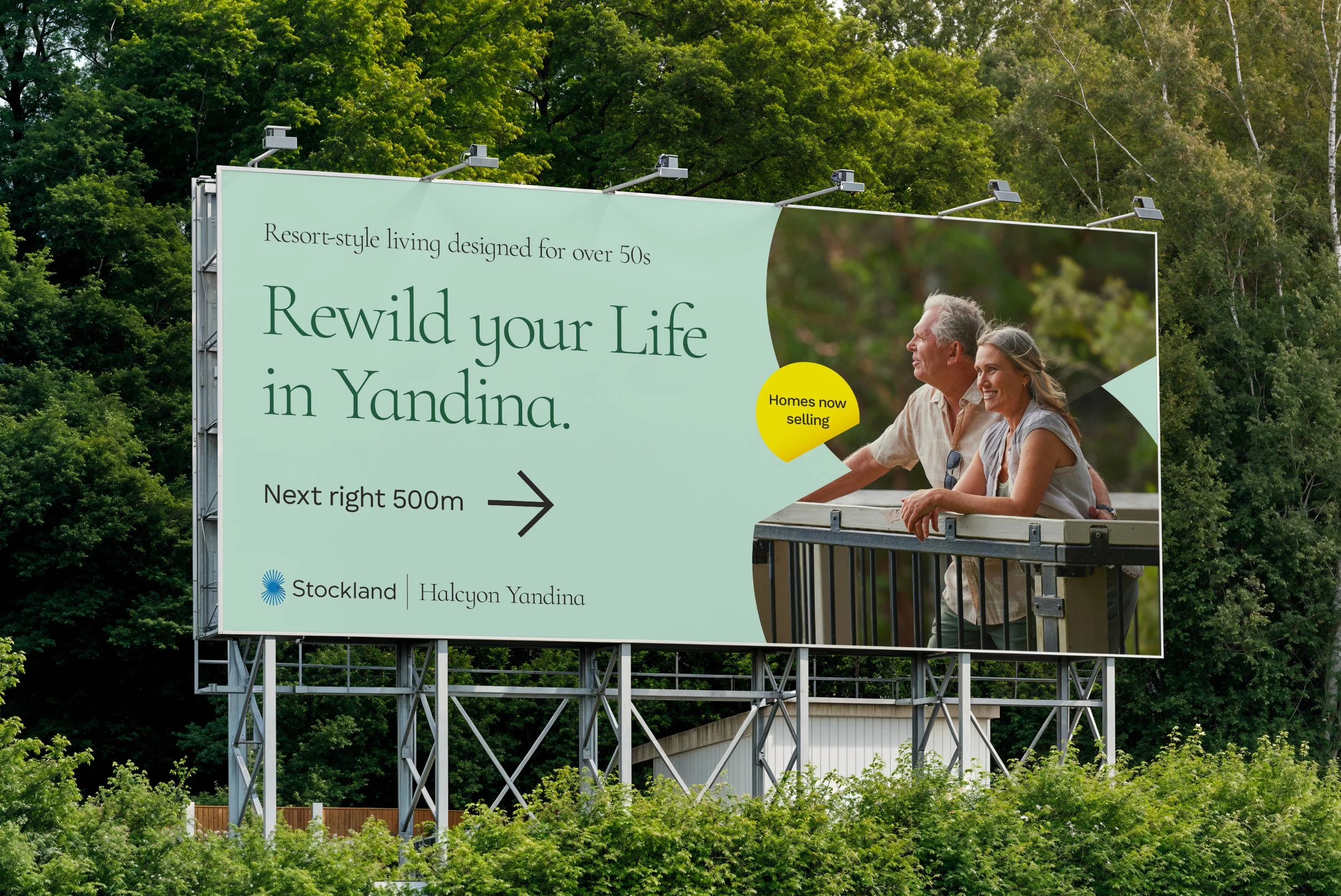 A large billboard advertising residential homes for people over 50 in Yandina, featuring a photo of an older couple on a balcony with trees in the background.