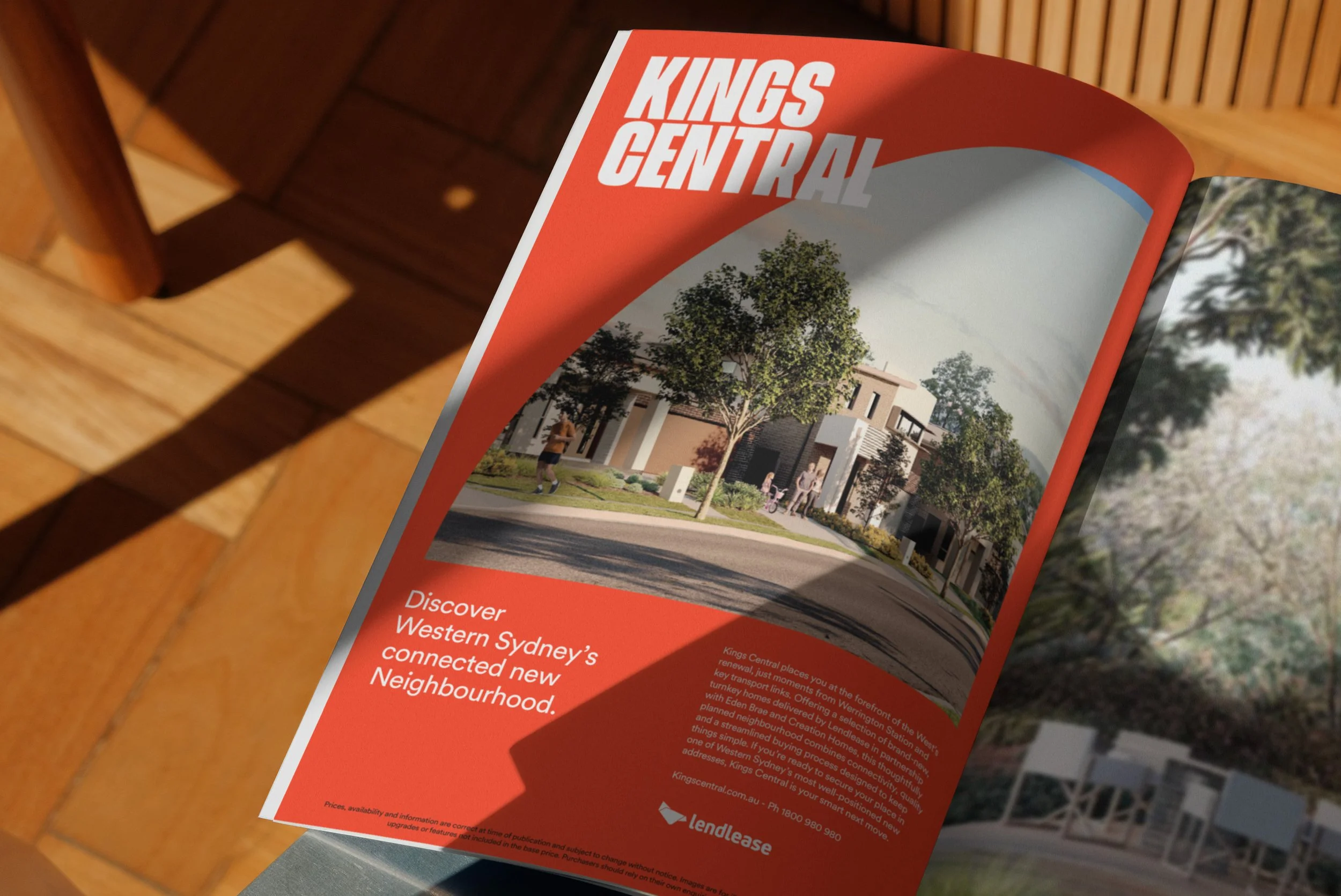 A red brochure titled 'Kings Central' resting on a wooden surface, featuring an illustration of a modern neighborhood with trees and people walking.