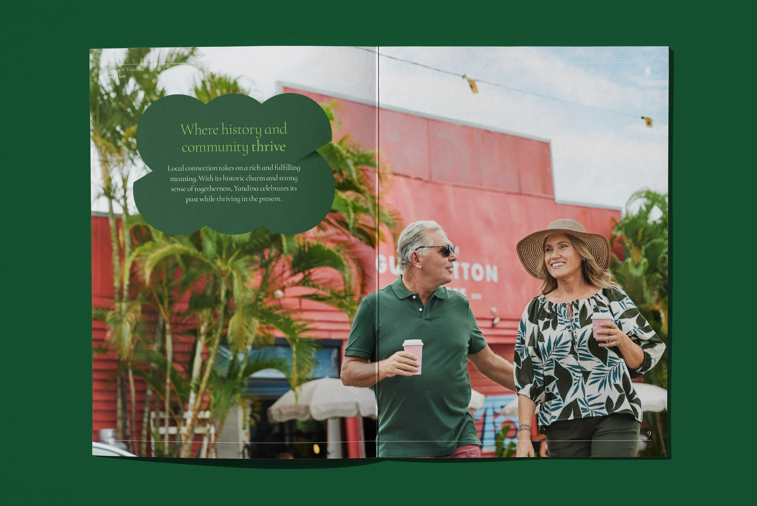 Two people, a man and a woman, walking outdoors with drinks in hand, smiling, and talking to each other, with a red building and greenery in the background.