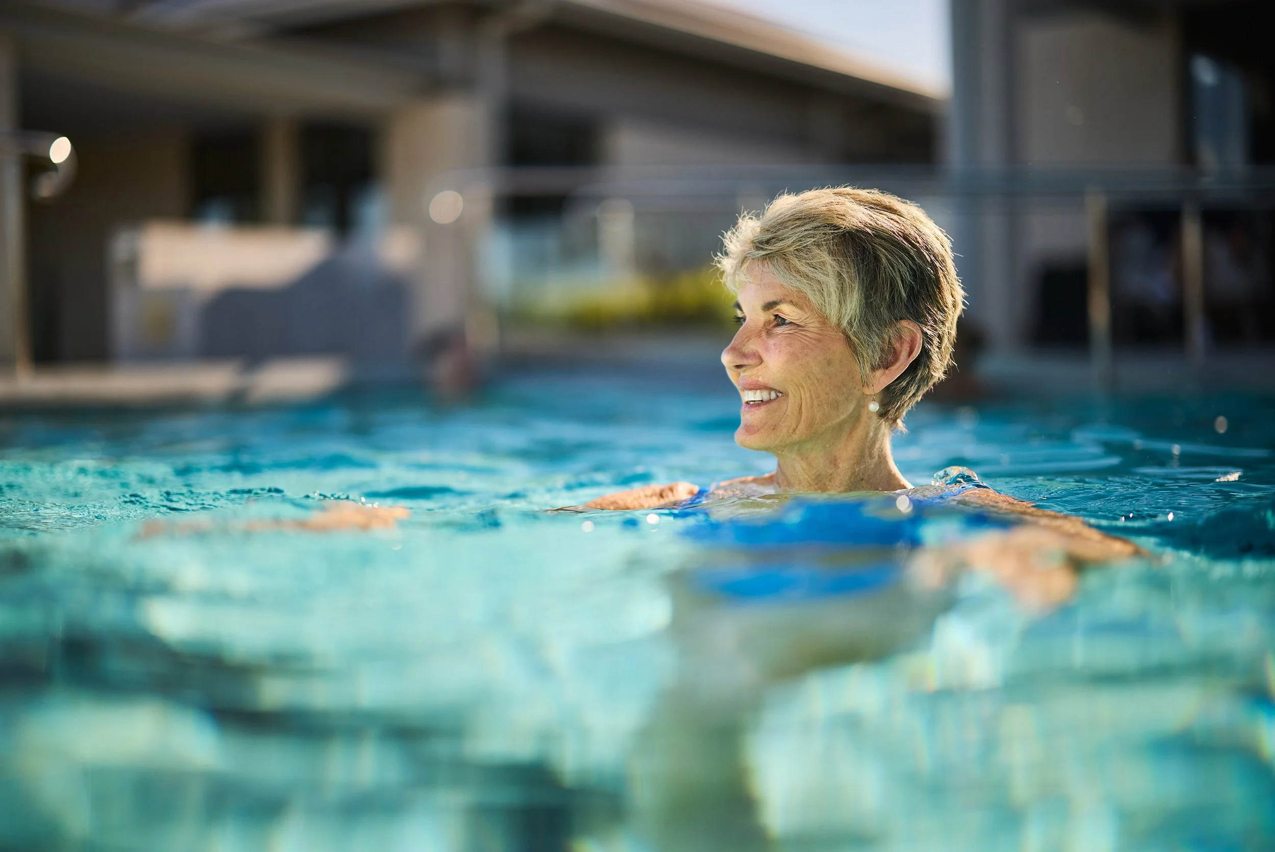 An older woman with short gray hair smiling and relaxing in a swimming pool.