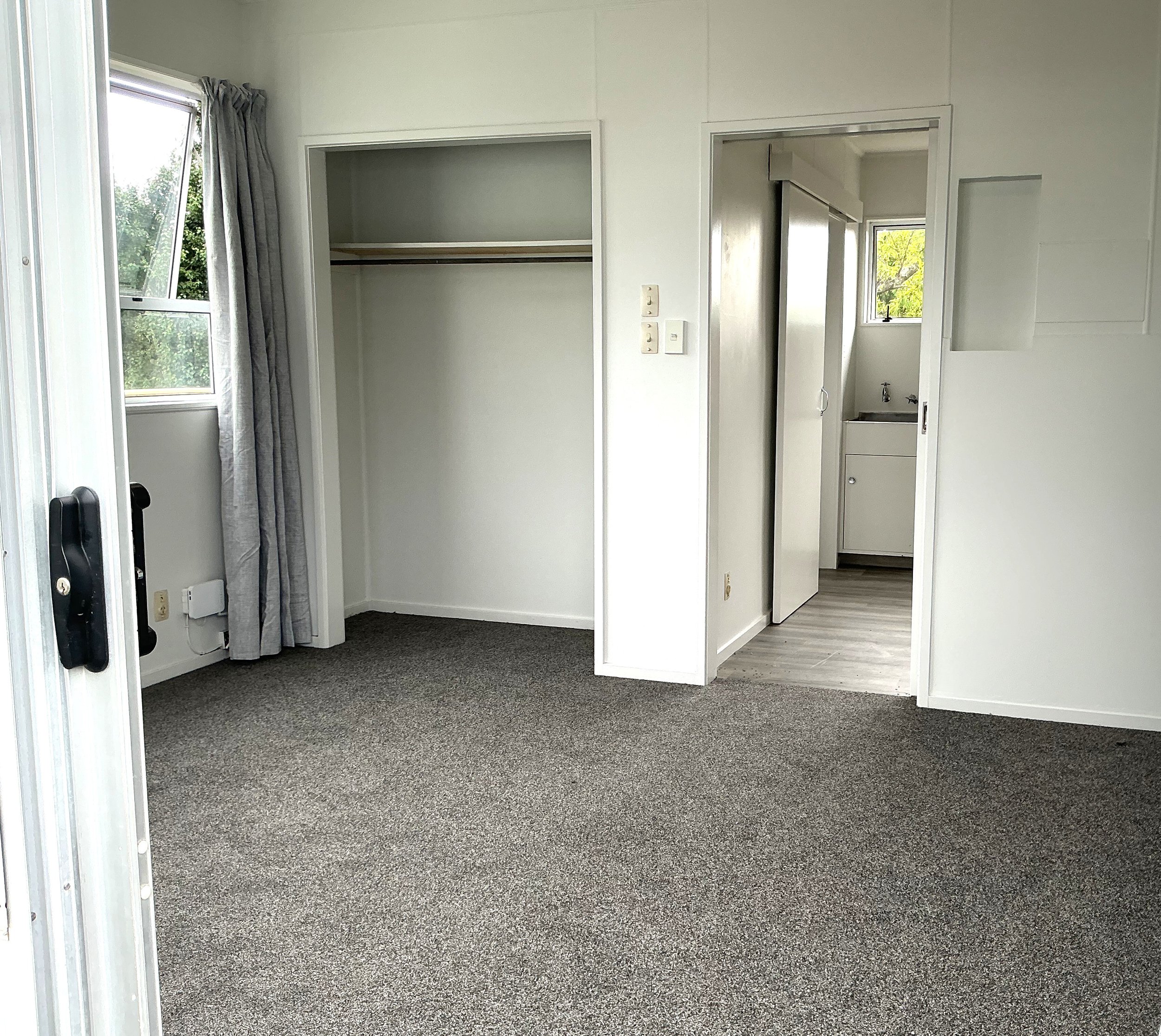 Empty room with gray carpet, closet with sliding door, and small laundry area with window.