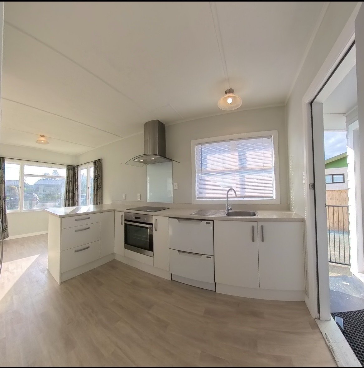 Modern kitchen with white cabinets, a built-in oven, a stovetop with a vent hood, a sink under a window, and a sliding door leading to an outdoor area.