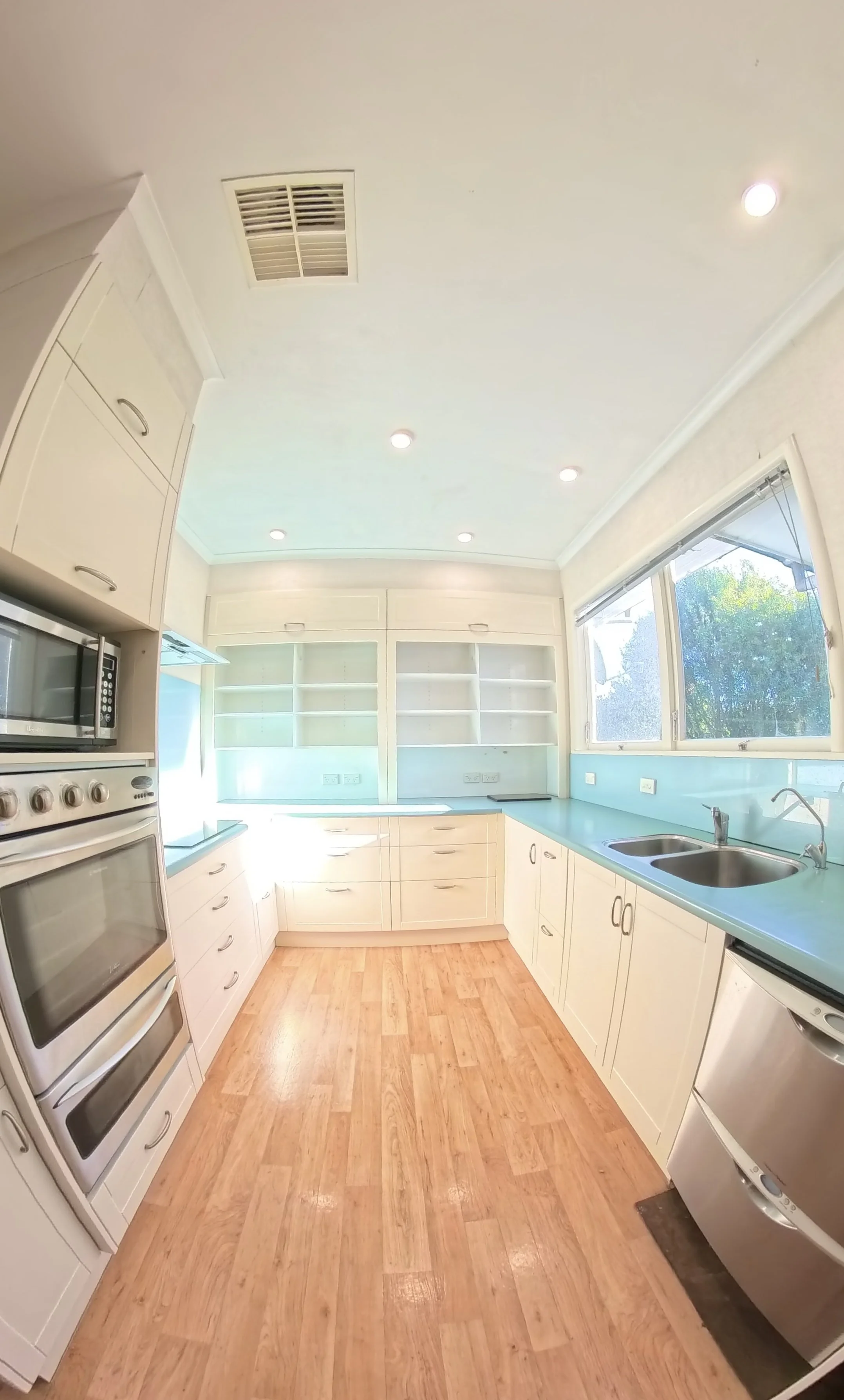 Bright kitchen with white cabinets, wood flooring, and a large window with blinds. Features a double sink, microwave, and stove.