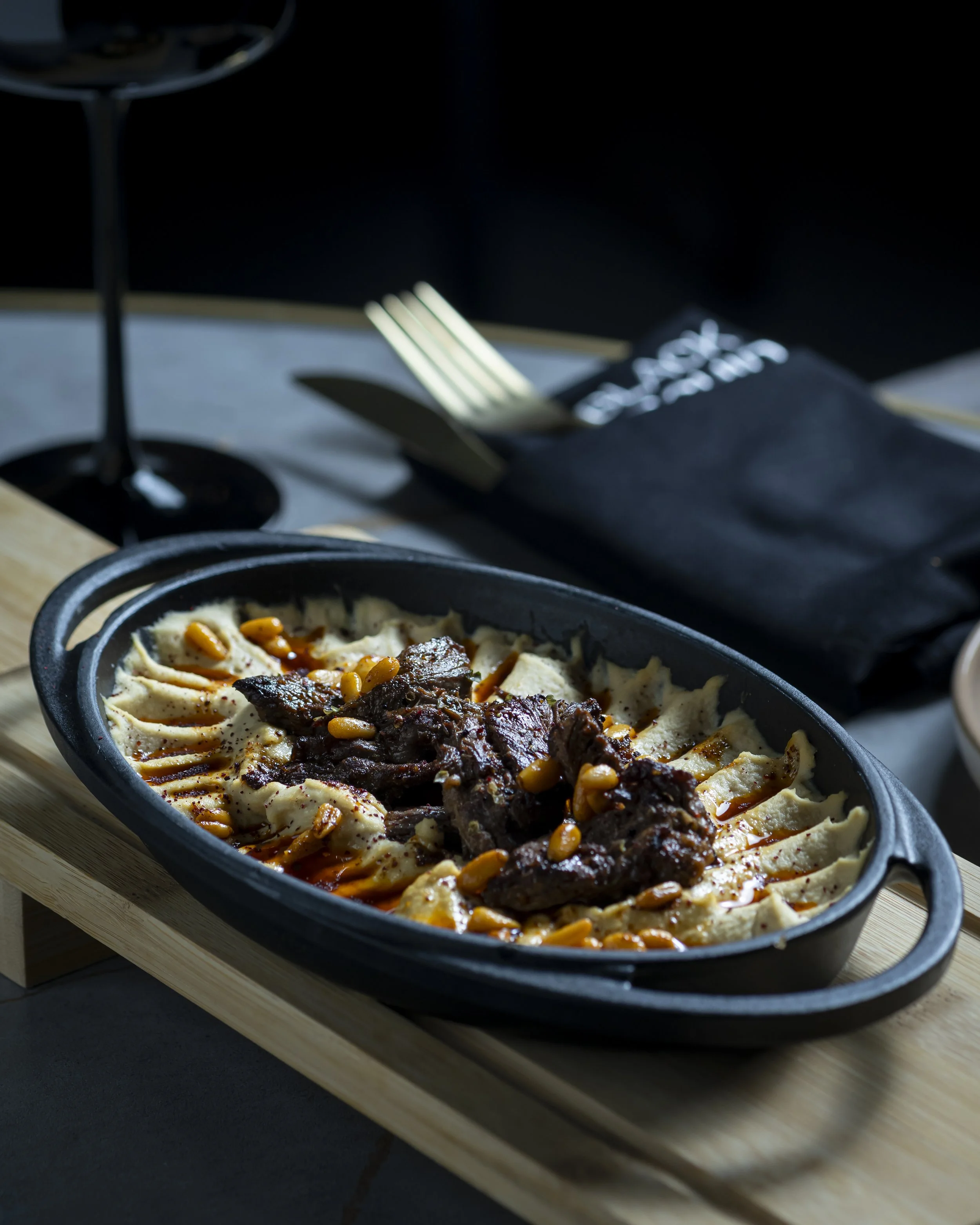 A black oval dish containing mashed potatoes topped with beef stew, garnished with corn and sauce, placed on a wooden board.