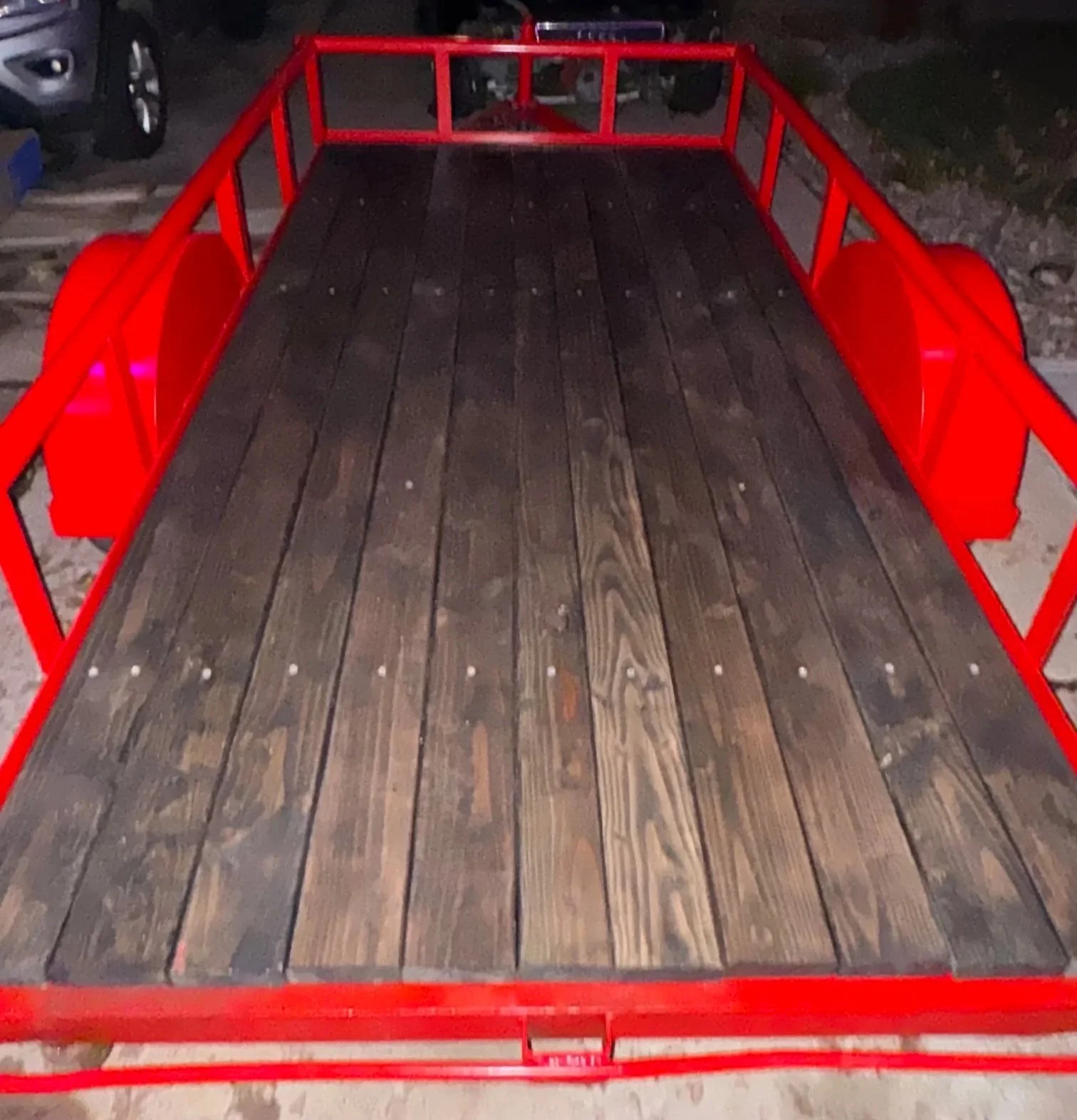 A flatbed trailer with a metal red frame and wooden planks on the bed.