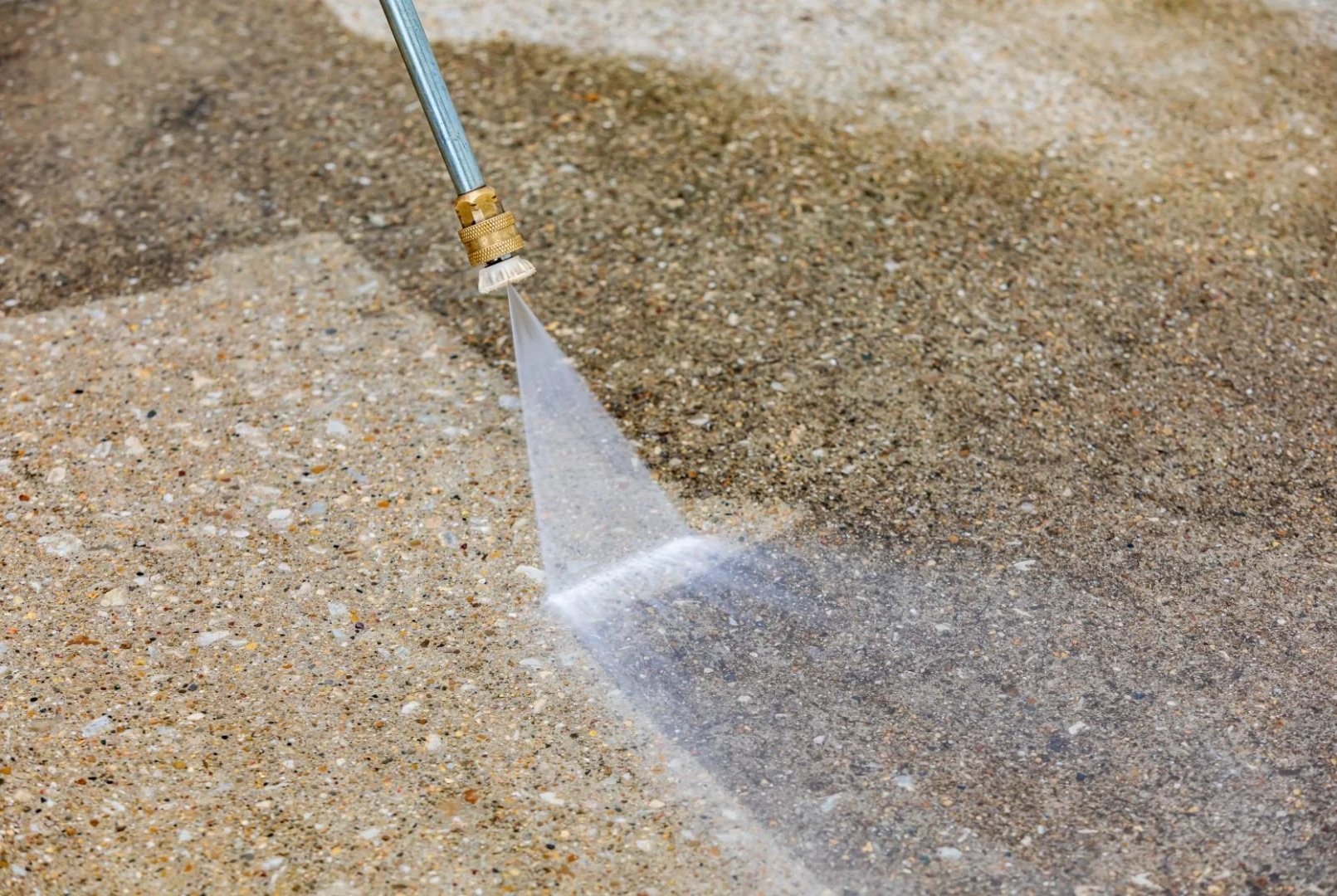 Close-up of a pressure washer wand cleaning a dirty concrete driveway, showing the clean line between washed and unwashed surface