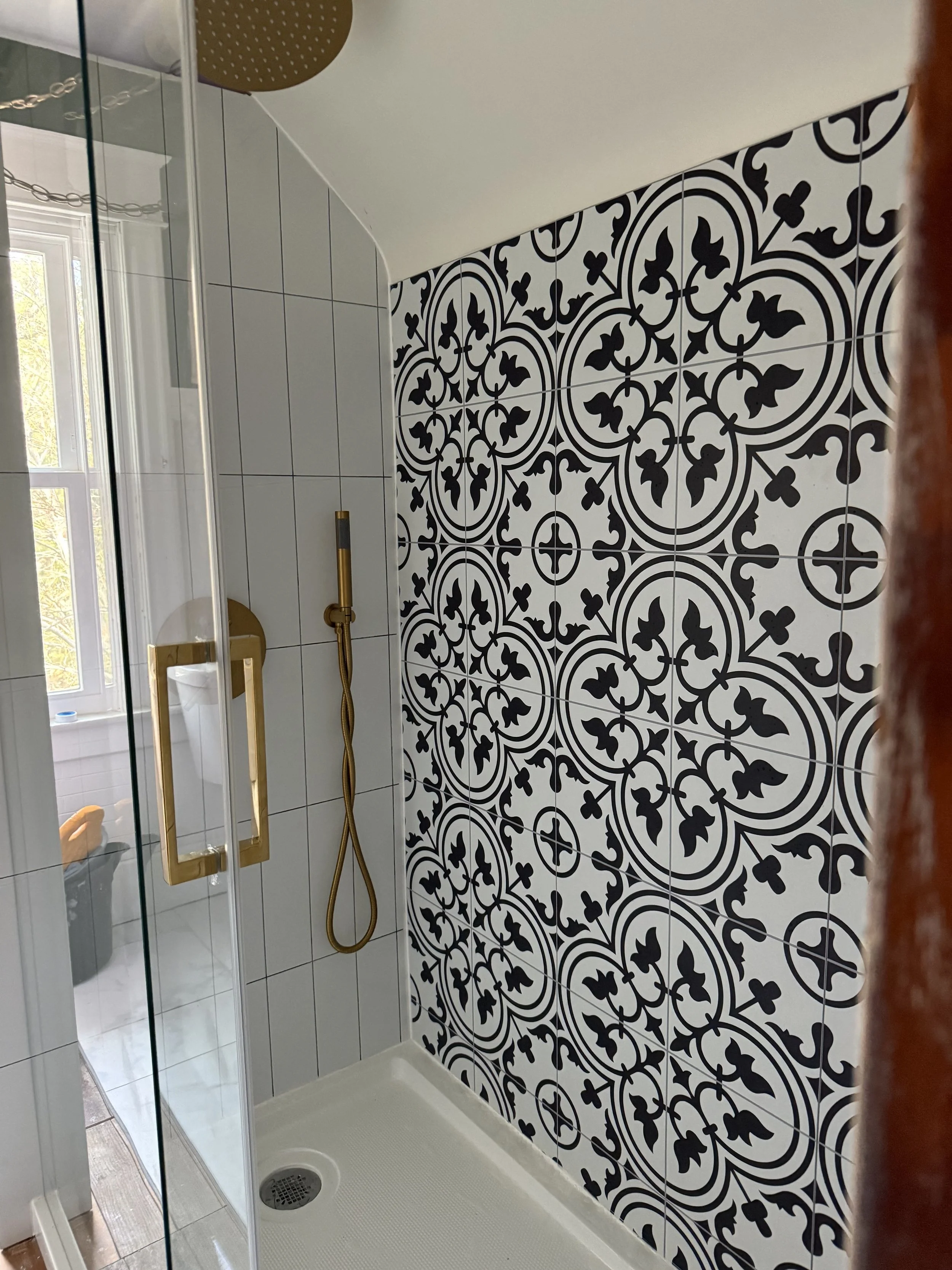 Shower area with patterned black and white wall tiles, a glass door, and a gold shower handle and fixtures.