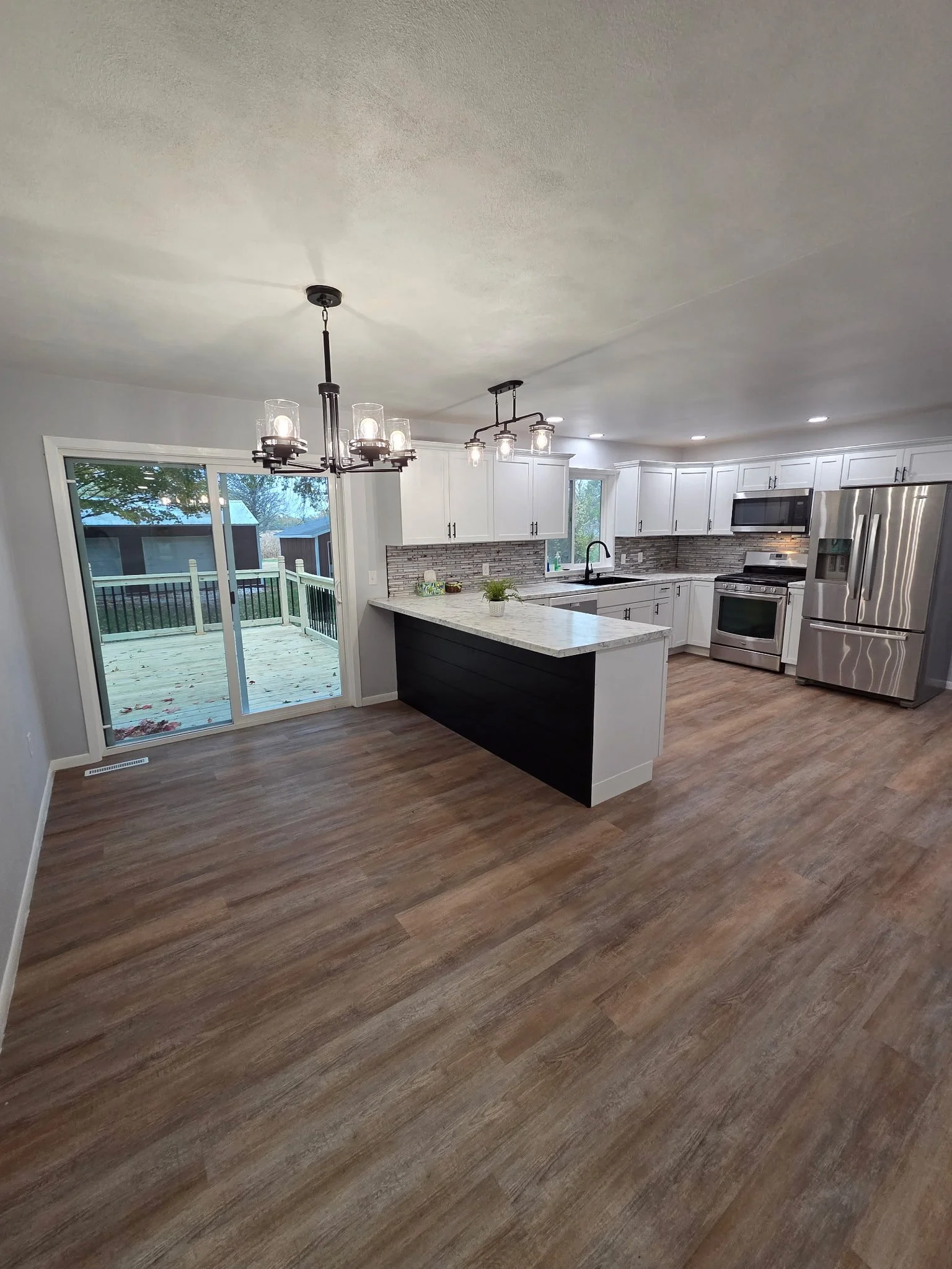 Modern kitchen with white cabinets, stainless steel appliances, and wood flooring. Modern black chandelier and pendant lights, sliding glass door leading to outdoor deck.