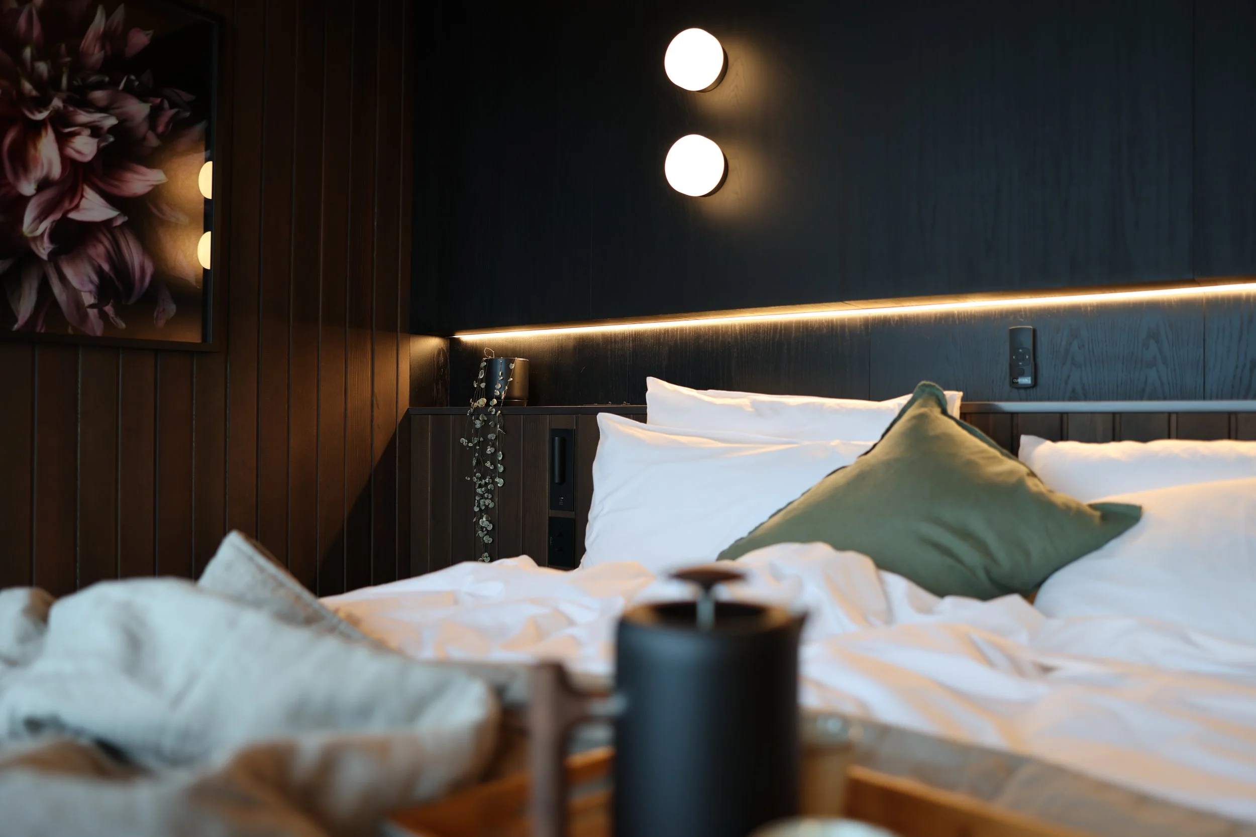 A luxurious king sized bed with dark wood and subtle headboard lighting.