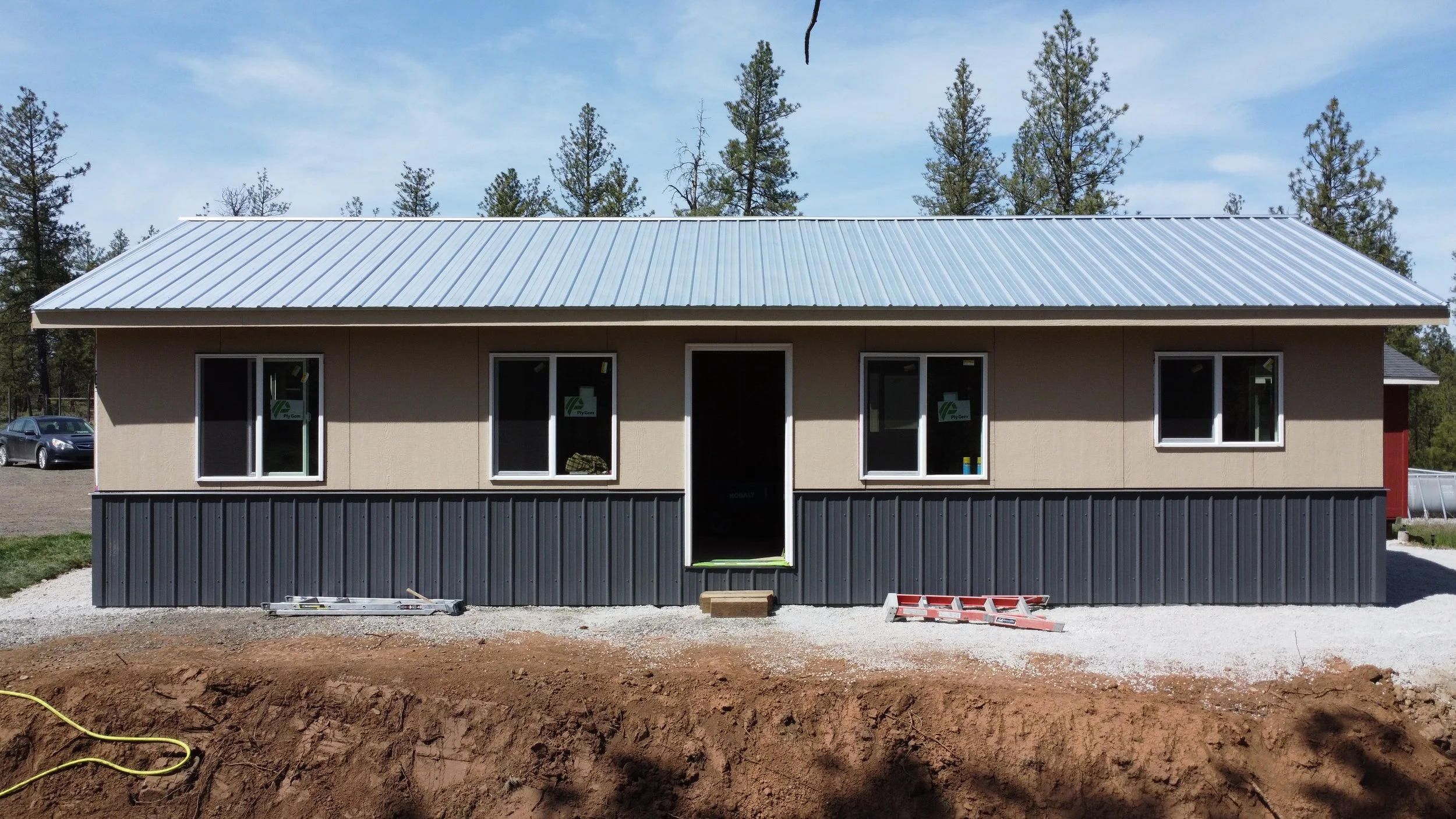 Modern residential pole barn construction featuring a sleek metal roof, durable two-tone siding with a dark corrugated wainscot, and integrated vinyl windows for a finished ADU workshop.