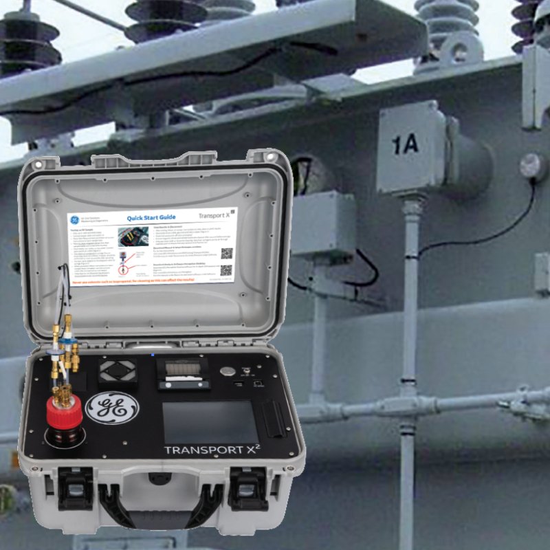 A portable testing device with a case labeled GE TRANSPORT X², connected to electrical equipment, atop electrical infrastructure such as insulators and transformers.