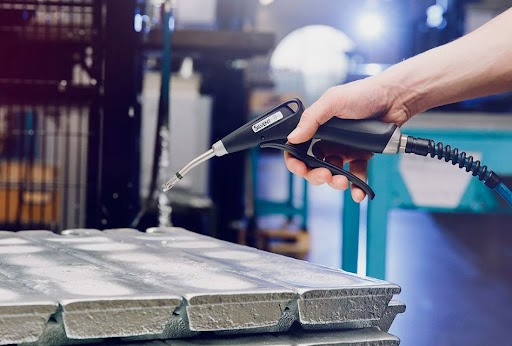 Person holding a handheld torch over a metal mold in a laboratory setting.