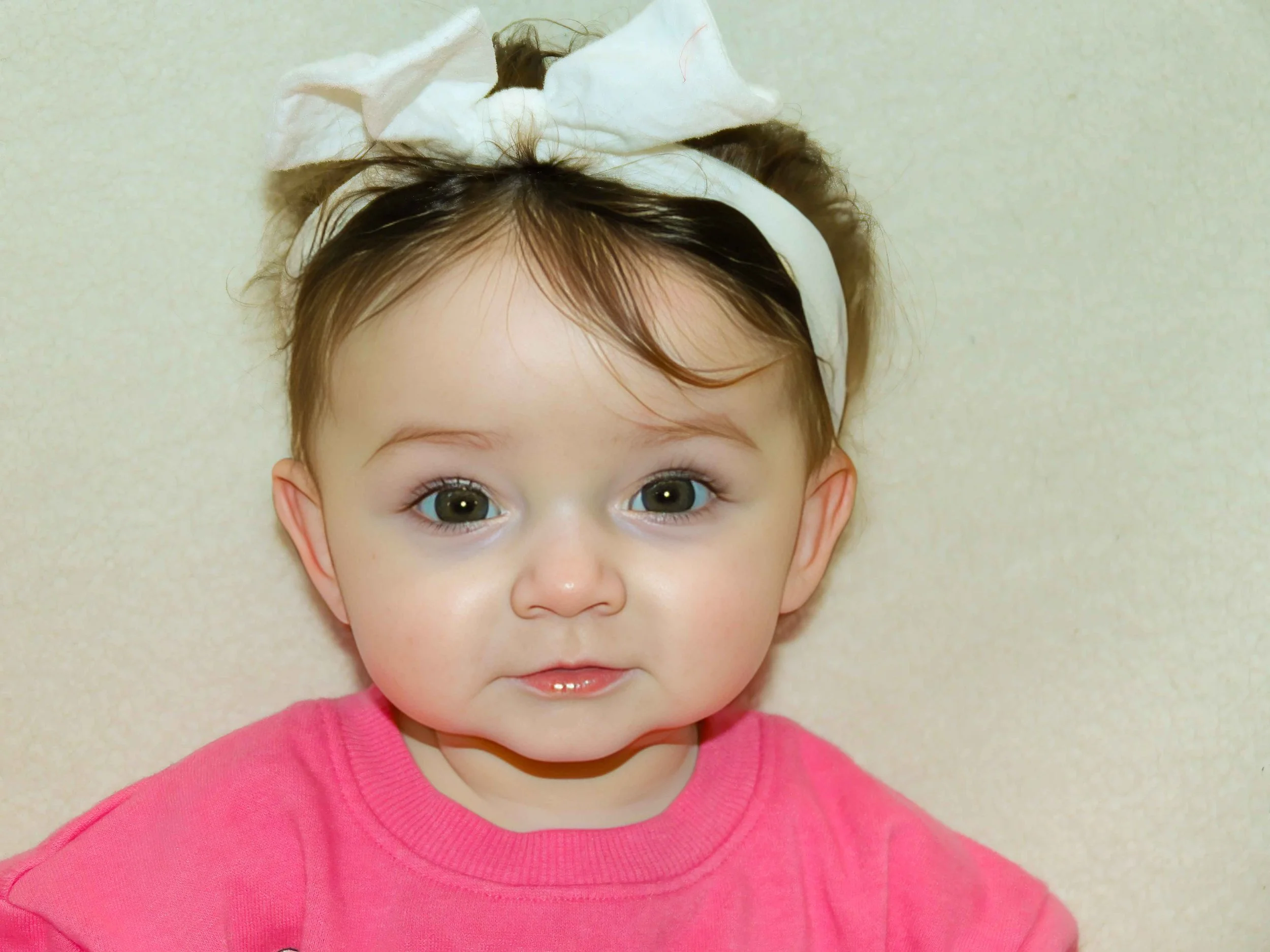A young girl with big eyes and light hair, wearing a pink shirt, has a tissue on her head and appears to have a cold or illness.