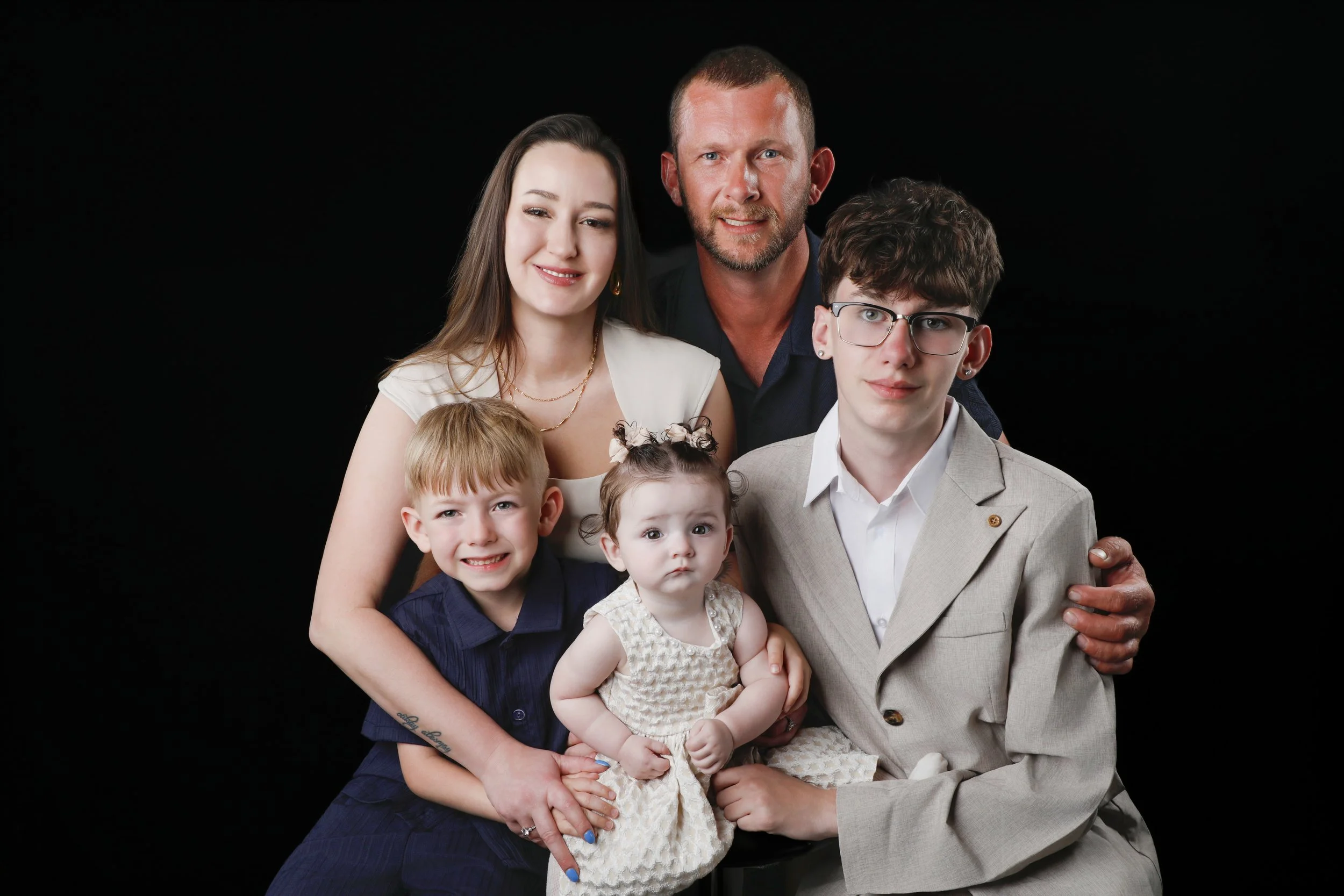 Family portrait of six members, including two adults and four children, against a black background.