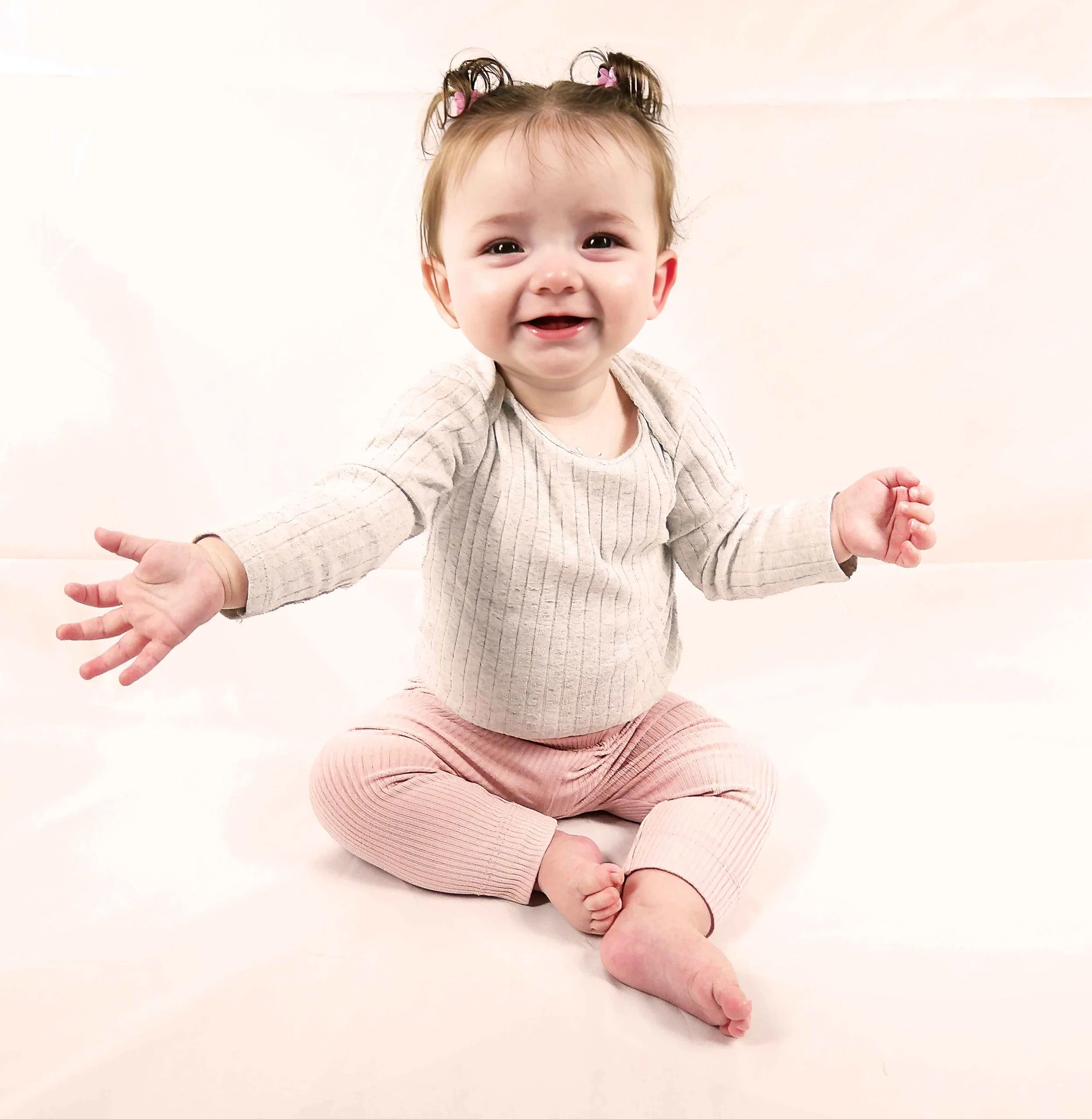 A smiling baby girl with butterfly clips in her hair, sitting on a white surface.