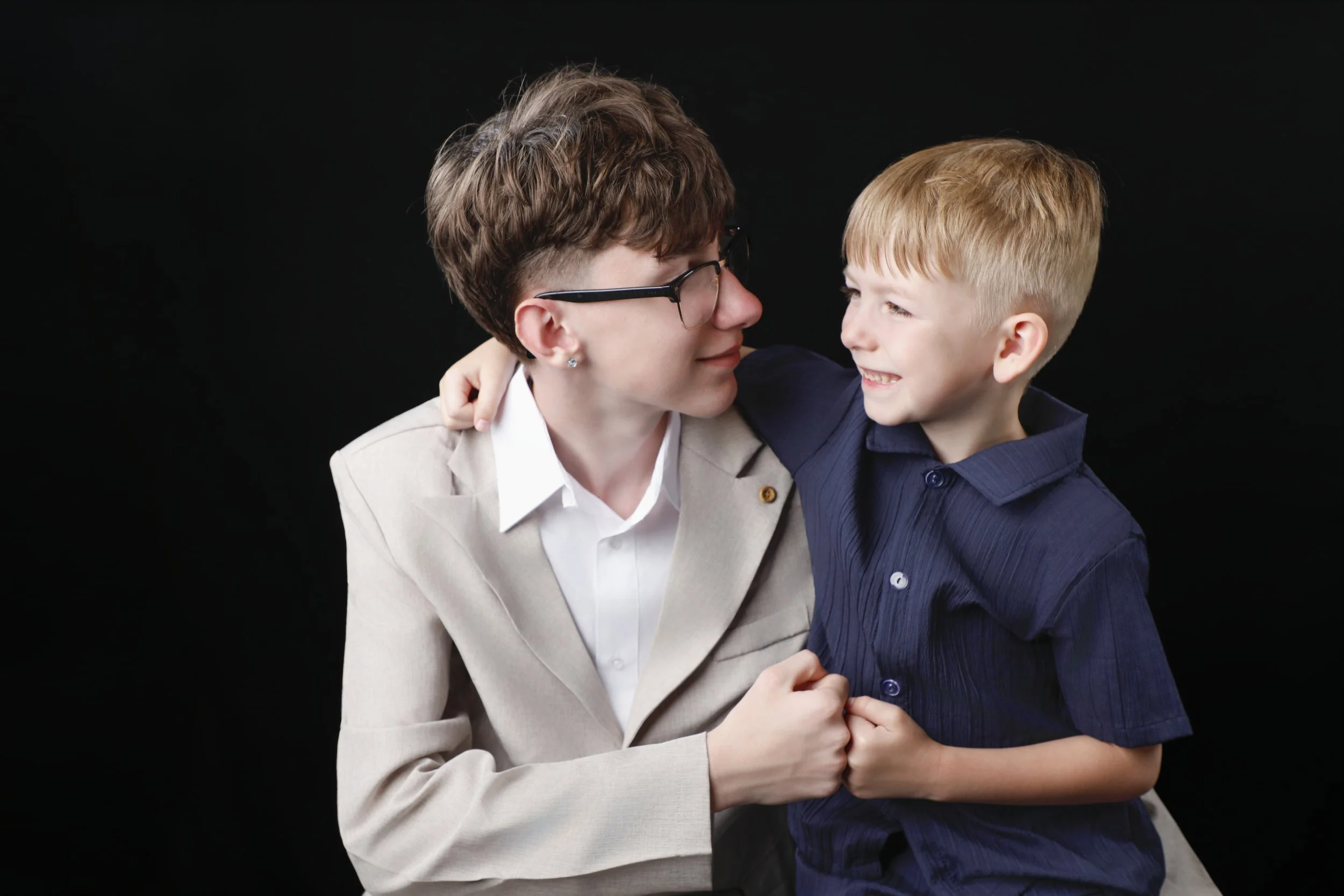 A woman and a young boy smiling and embracing each other against a black background.