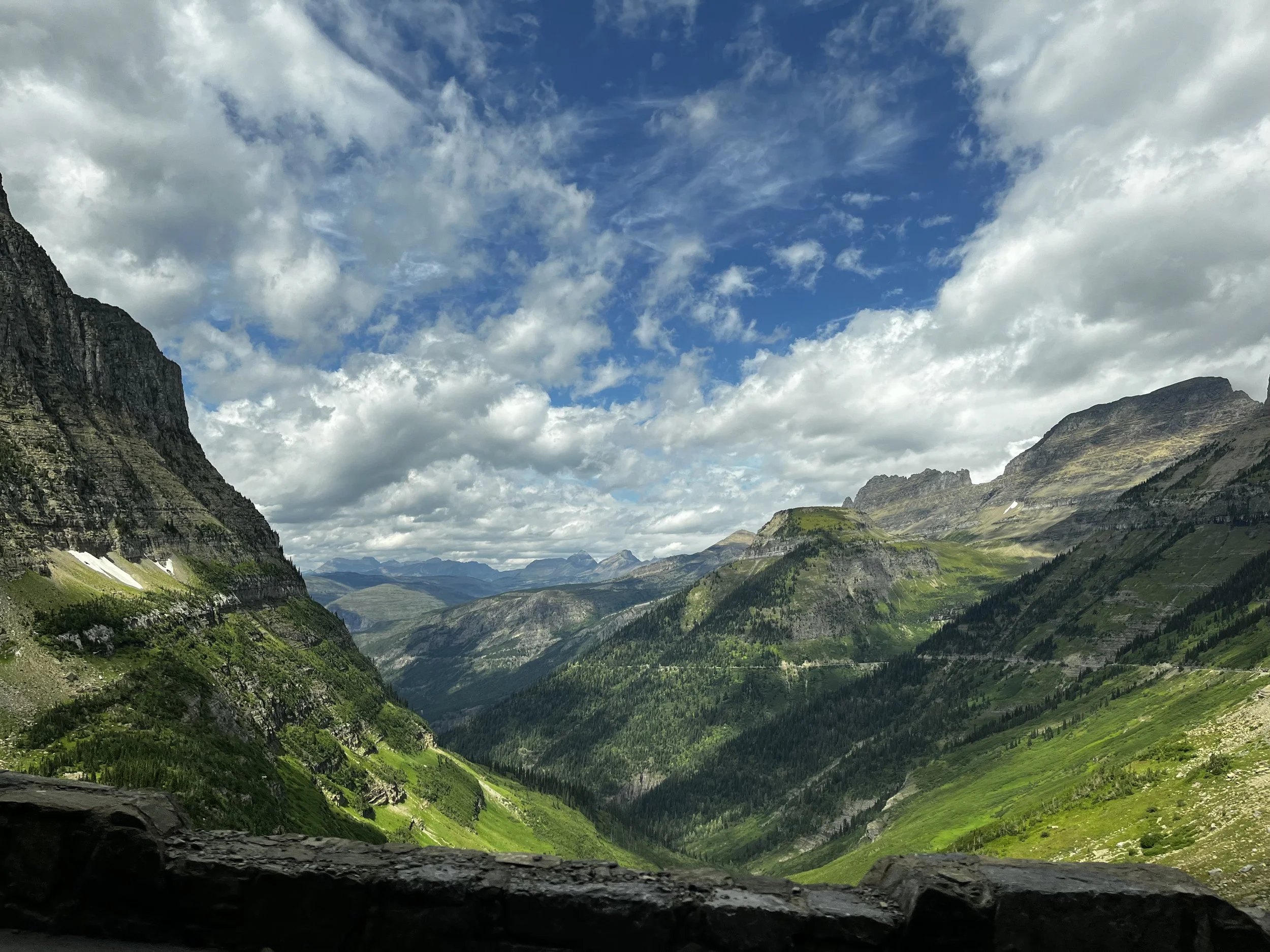 Scenic view of a mountainous valley with lush green slopes and rocky peaks under a partly cloudy sky.
