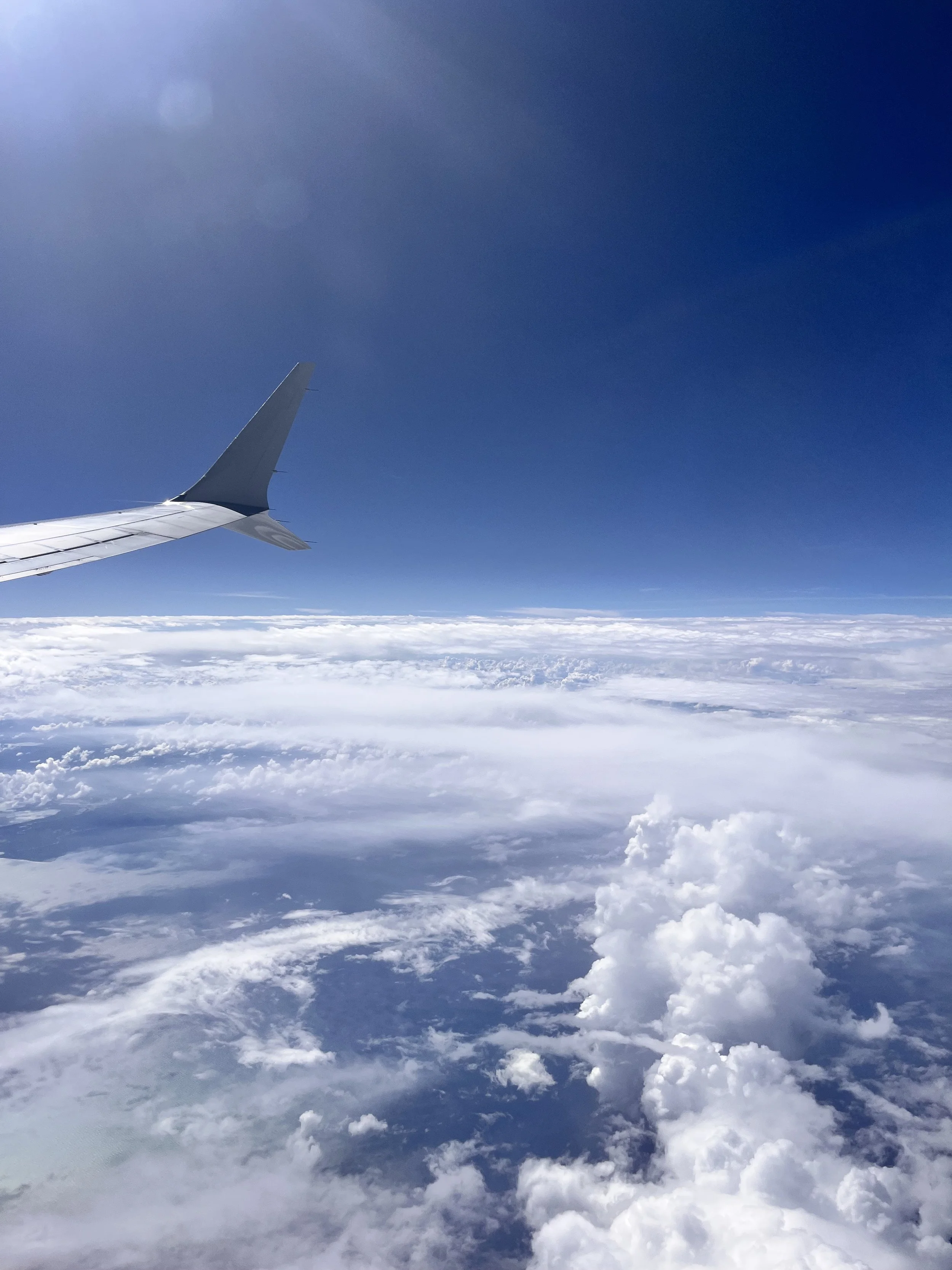 View of airplane wing against a clear blue sky with scattered clouds below.