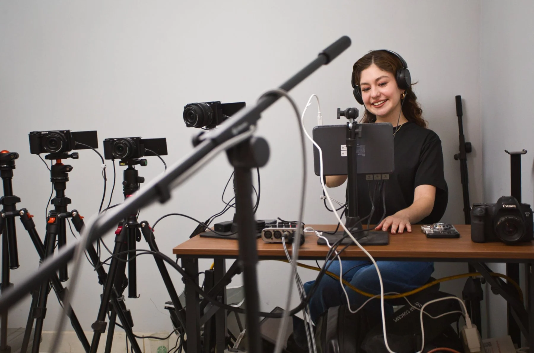 Mujer sonriendo con gafas y auriculares frente a una mesa con cámaras, trípodes y equipo de grabación en un estudio