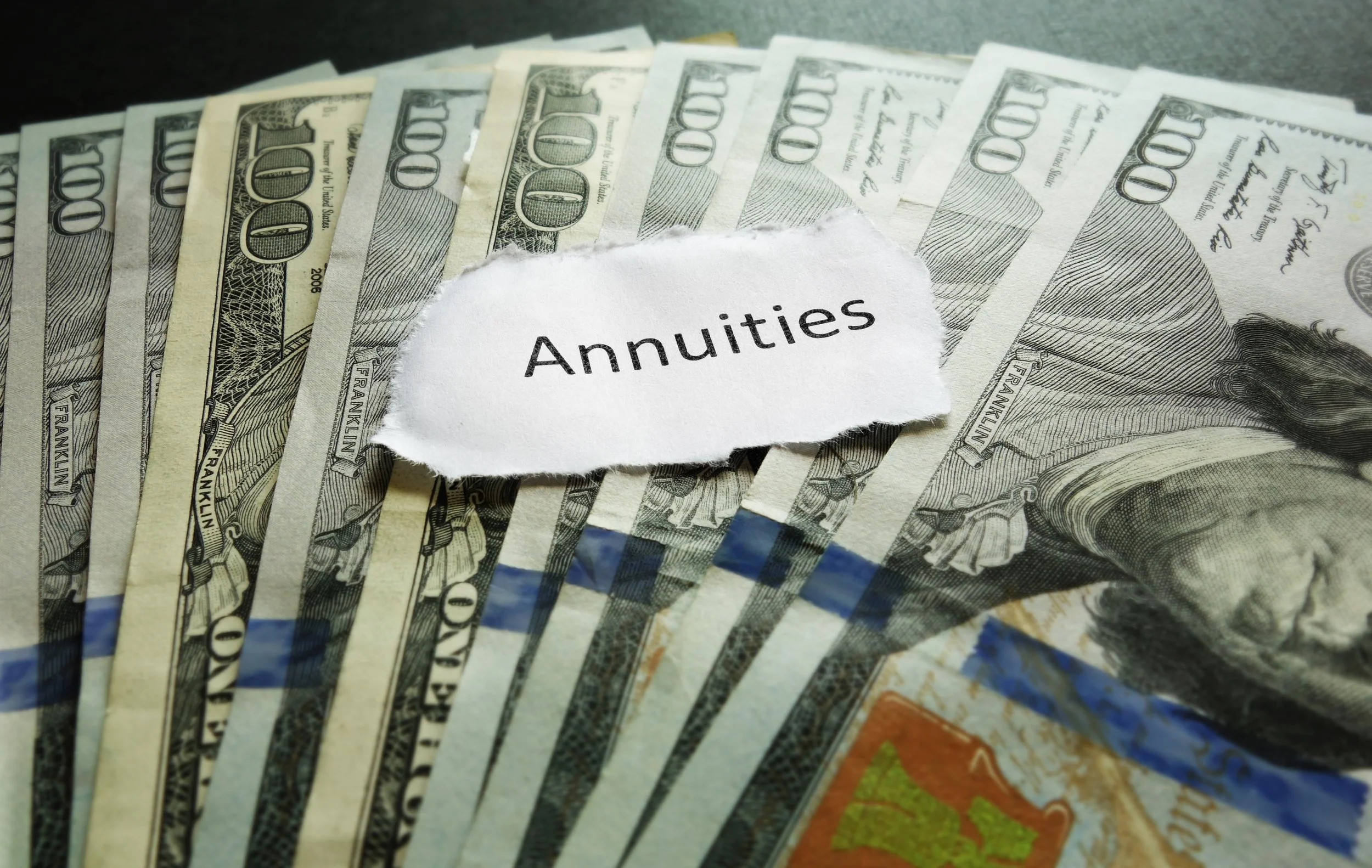 Several US 100-dollar bills scattered with a torn piece of paper labeled 'Annuities' on top.