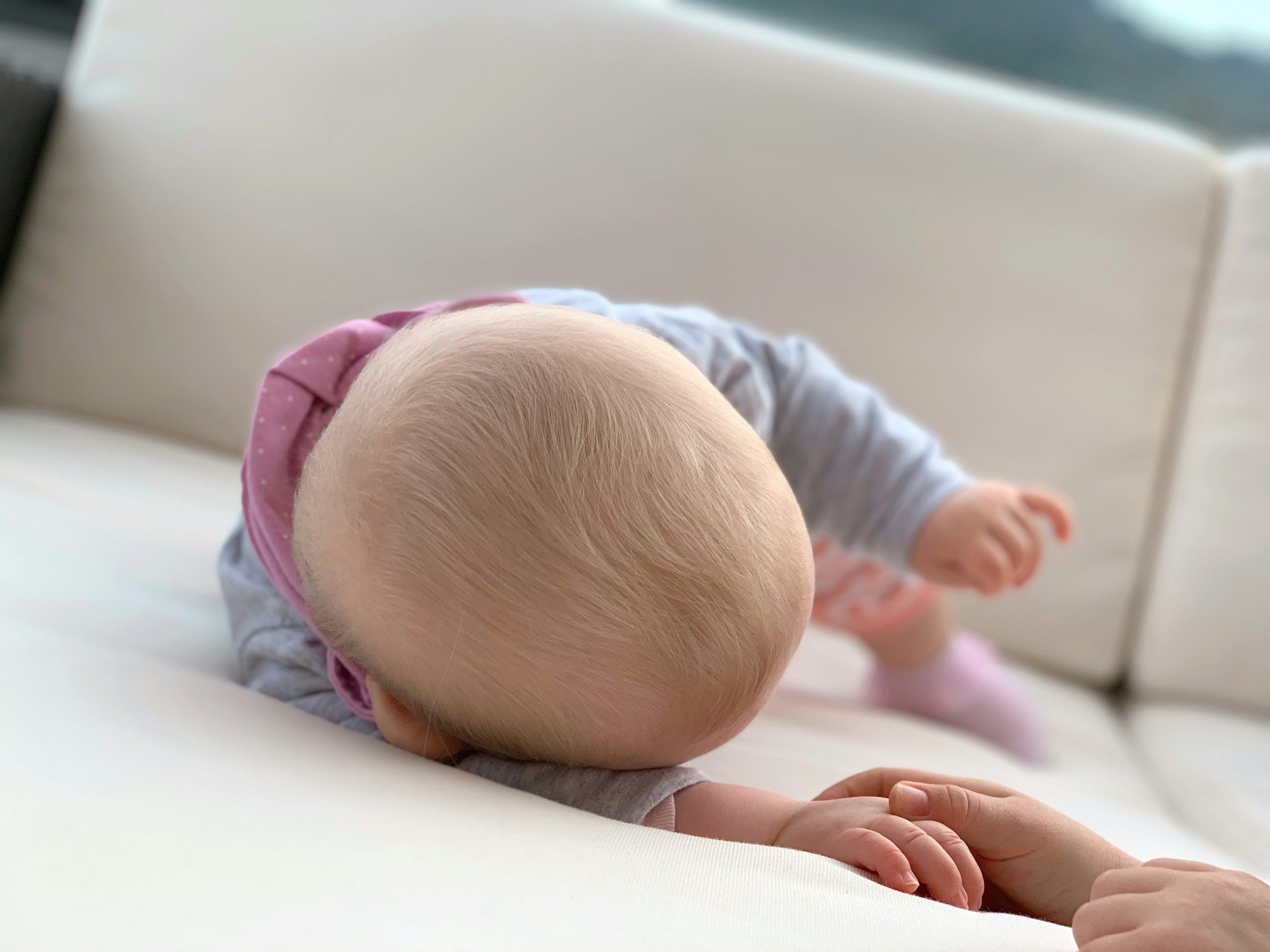Close-up of a baby crawling on a white surface, wearing a pink and gray outfit, with a focus on the baby's bald head and tiny hand.