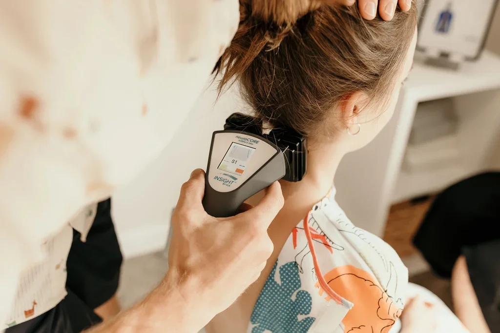 A person holding a skin thermometer against a woman's neck during a consultation or medical check-up, in a room with a computer and medical supplies.