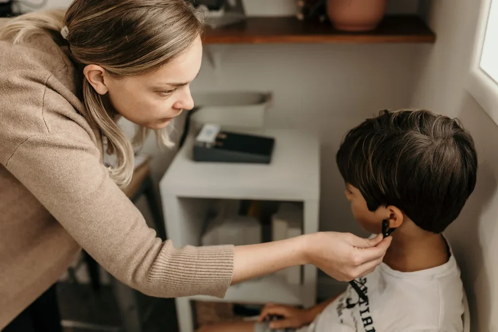 Woman giving a boy a haircut at home near a window.