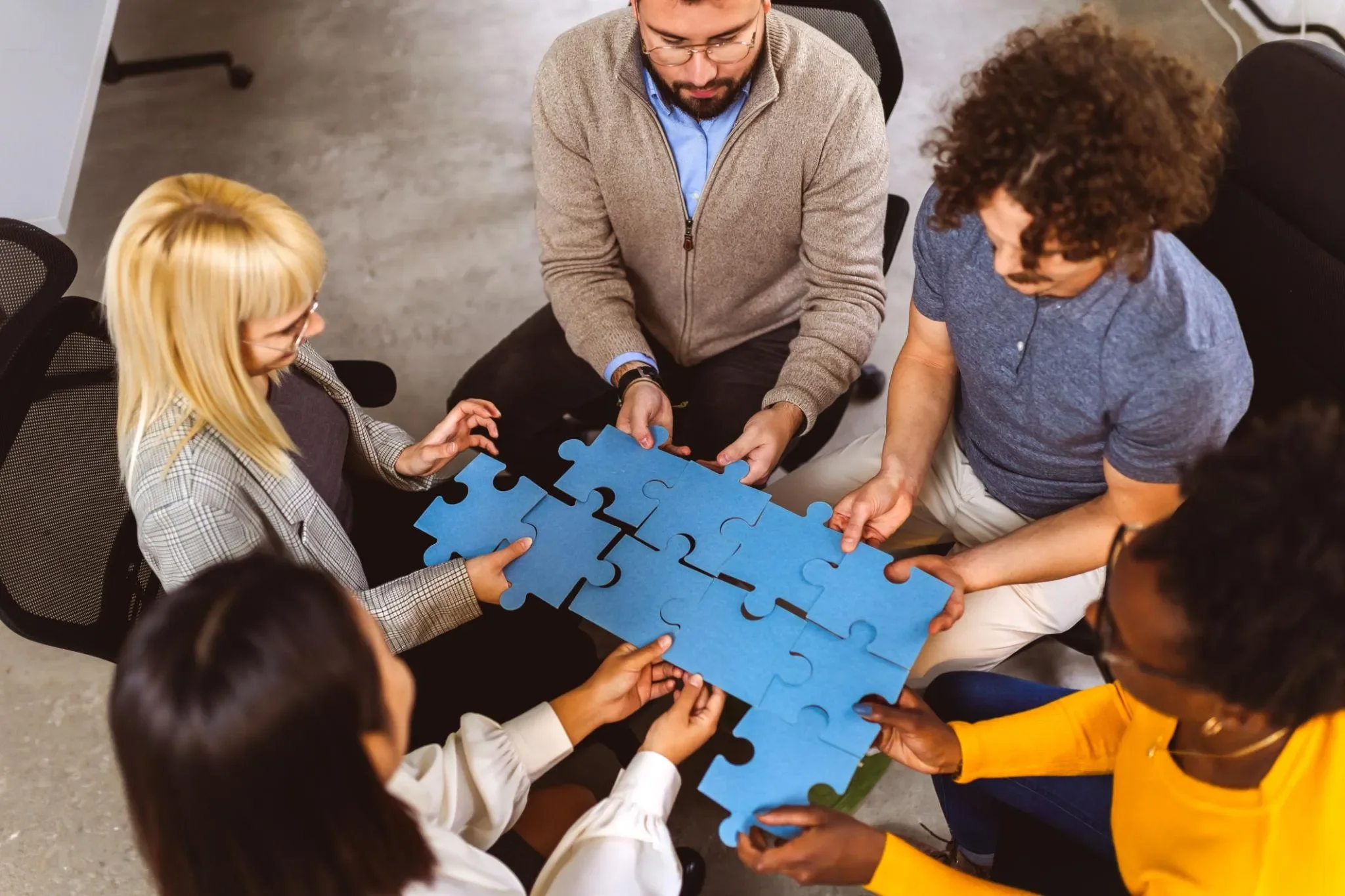Five people work together to fit oversized blue puzzle pieces together.