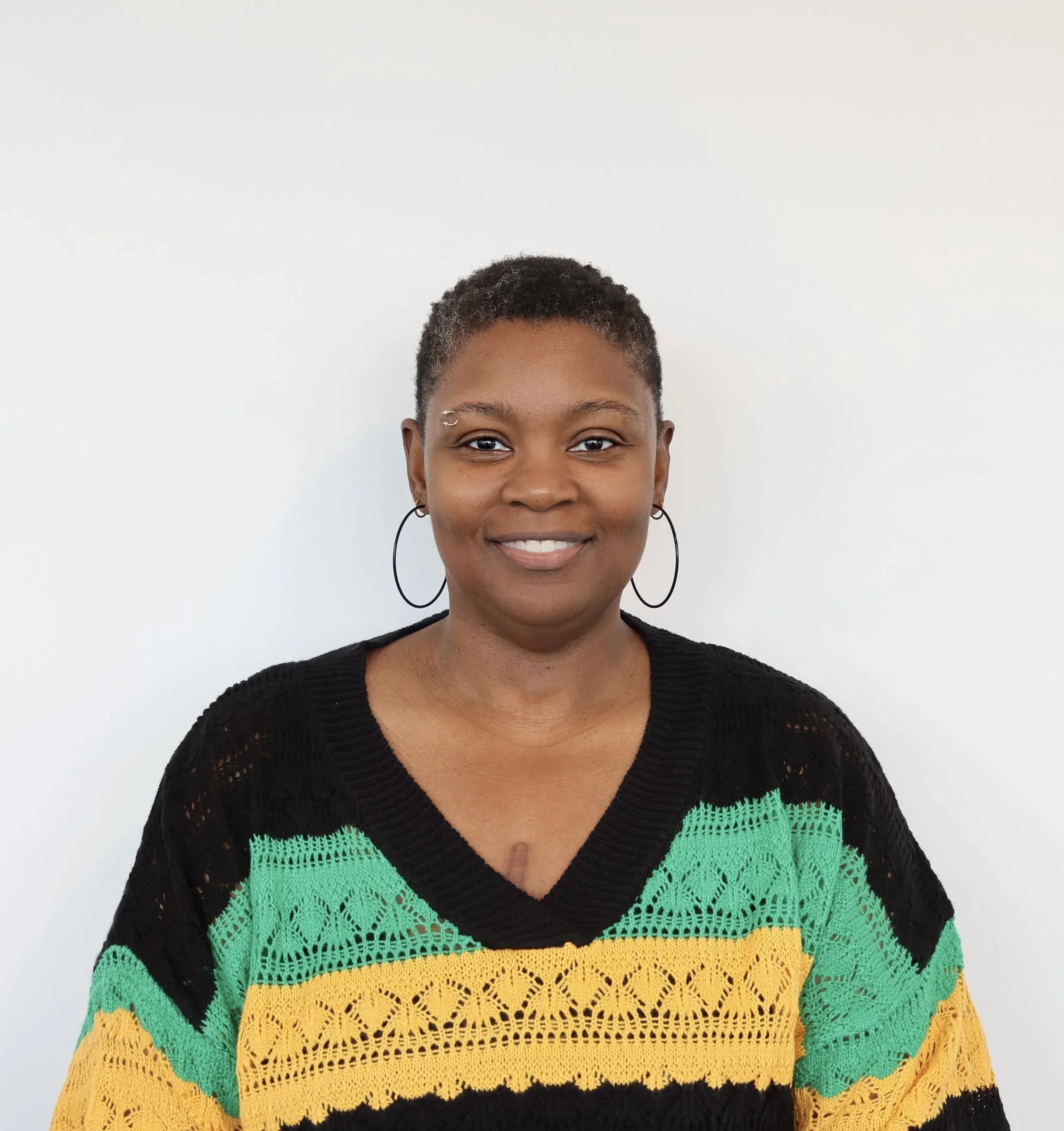 Professional headshot of a smiling woman with short hair wearing a black, green, and yellow sweater.