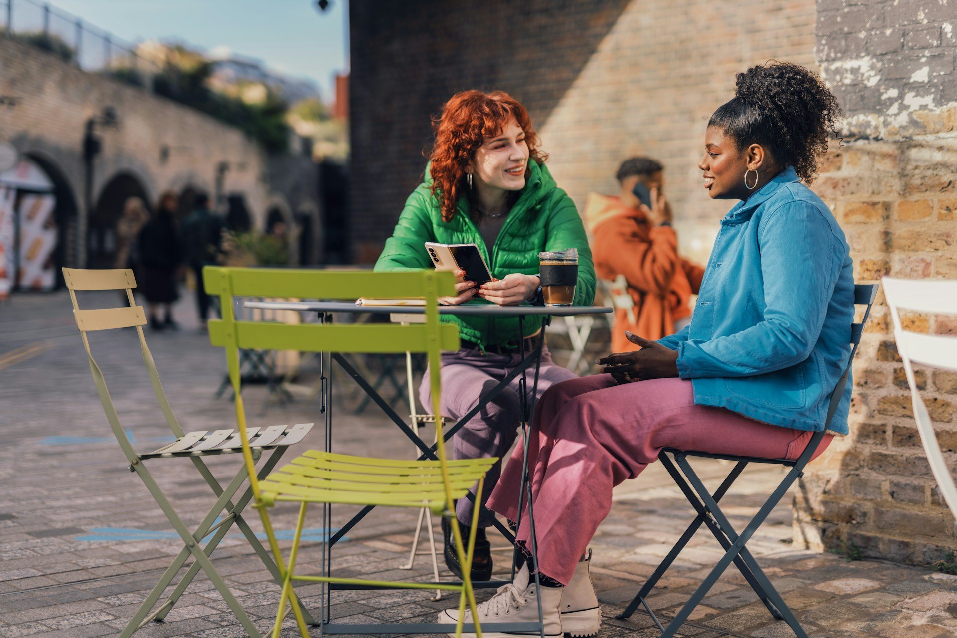 Two women sitting at an outdoor table and talking together.