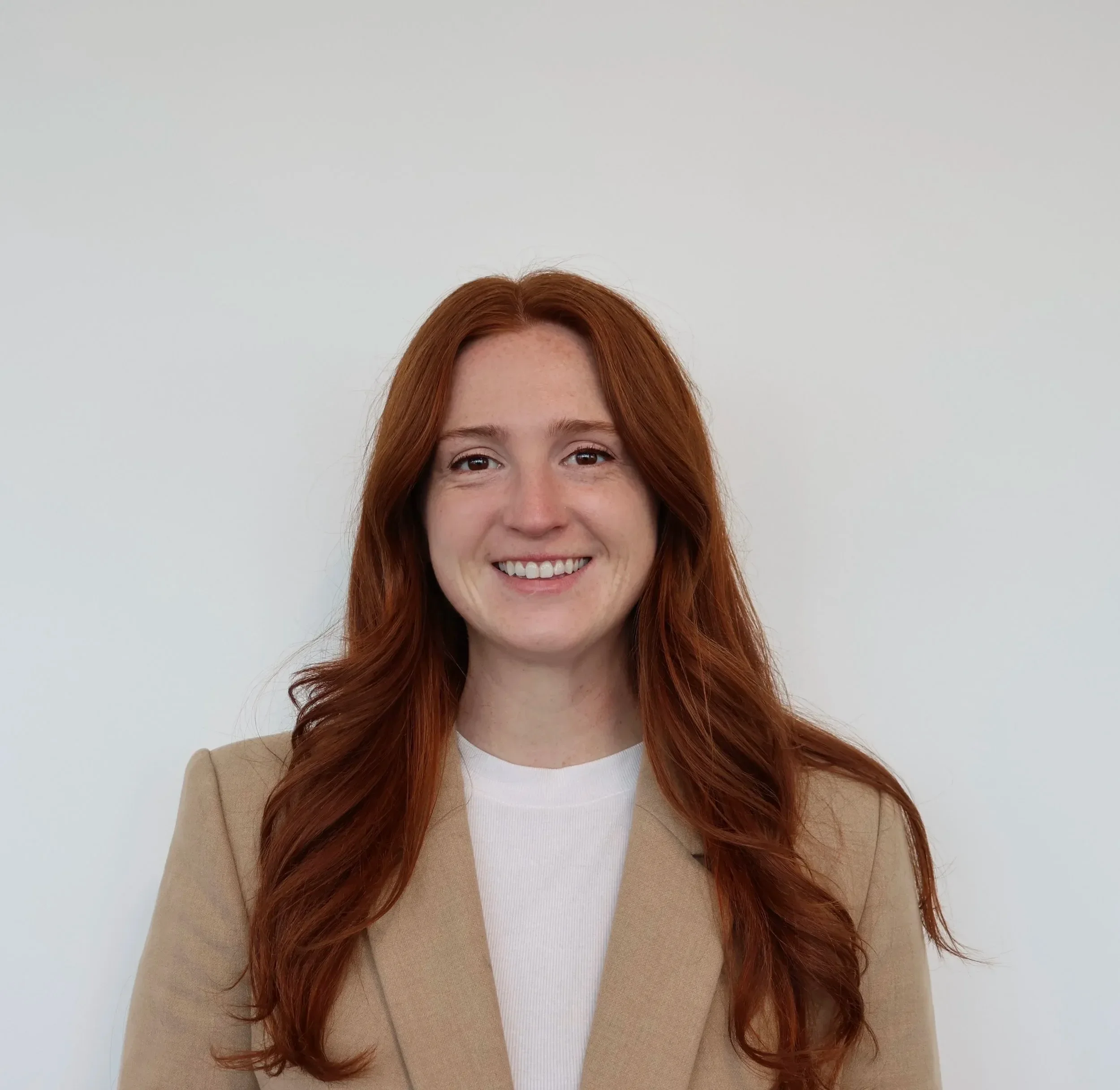 Professional headshot of a smiling woman with long red hair wearing a tan blazer.