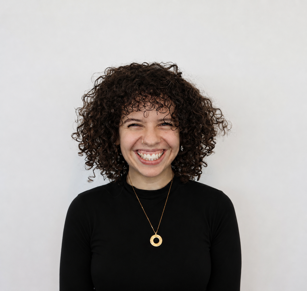 Professional headshot of a smiling woman with curly dark hair wearing a black top.