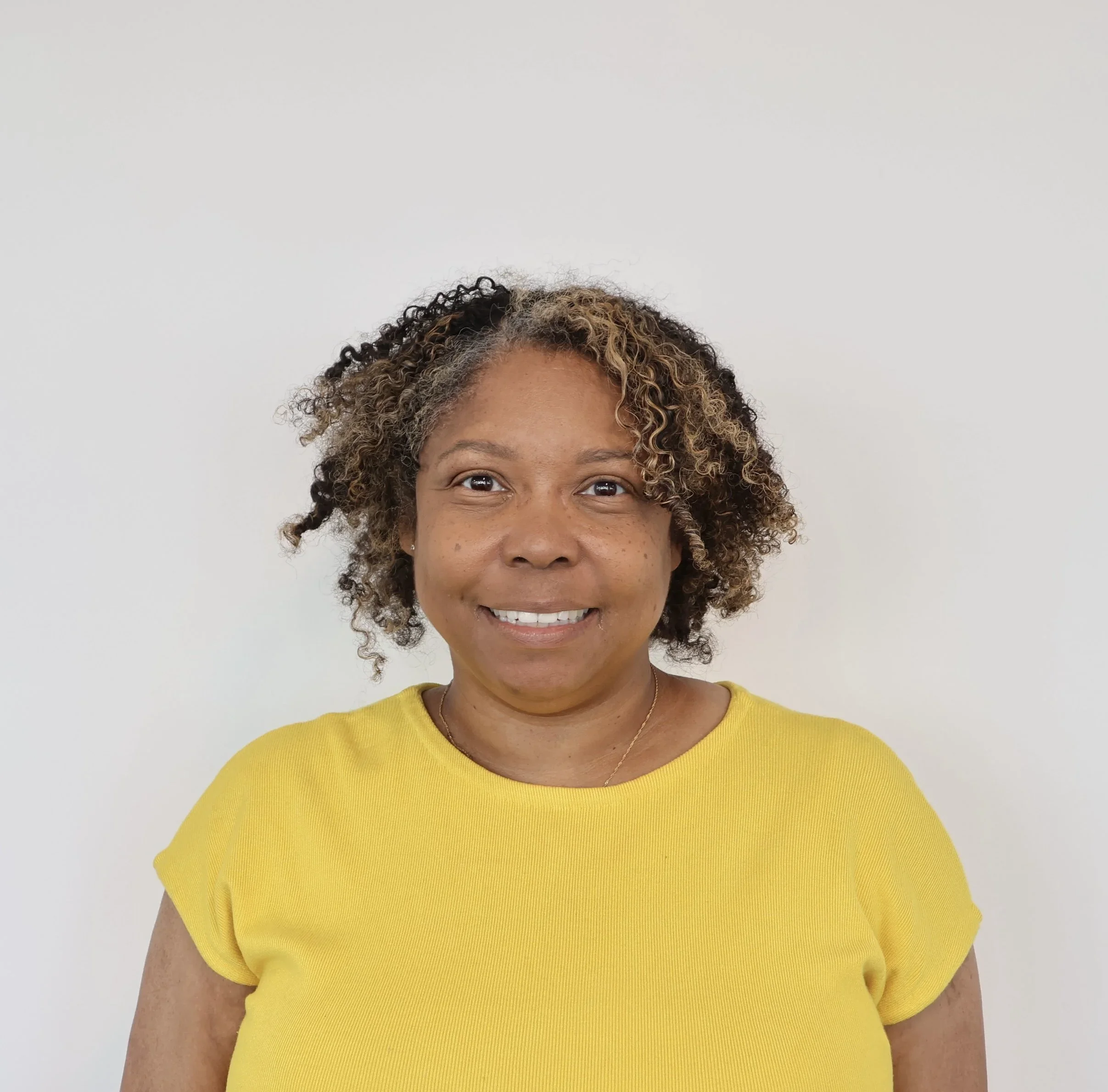 Professional headshot of a smiling woman with short curly hair wearing a yellow top.