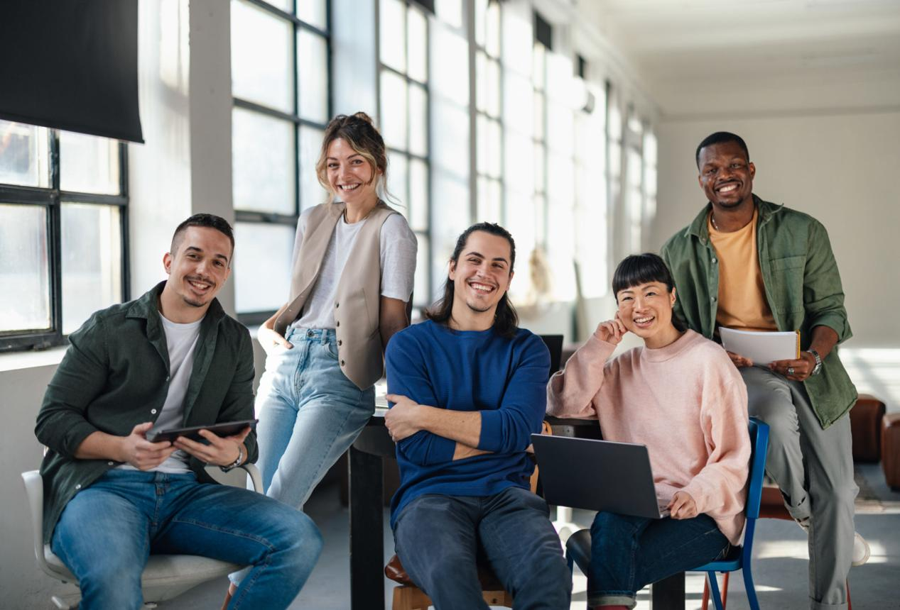 Five people smiling together in a bright collaborative workspace.