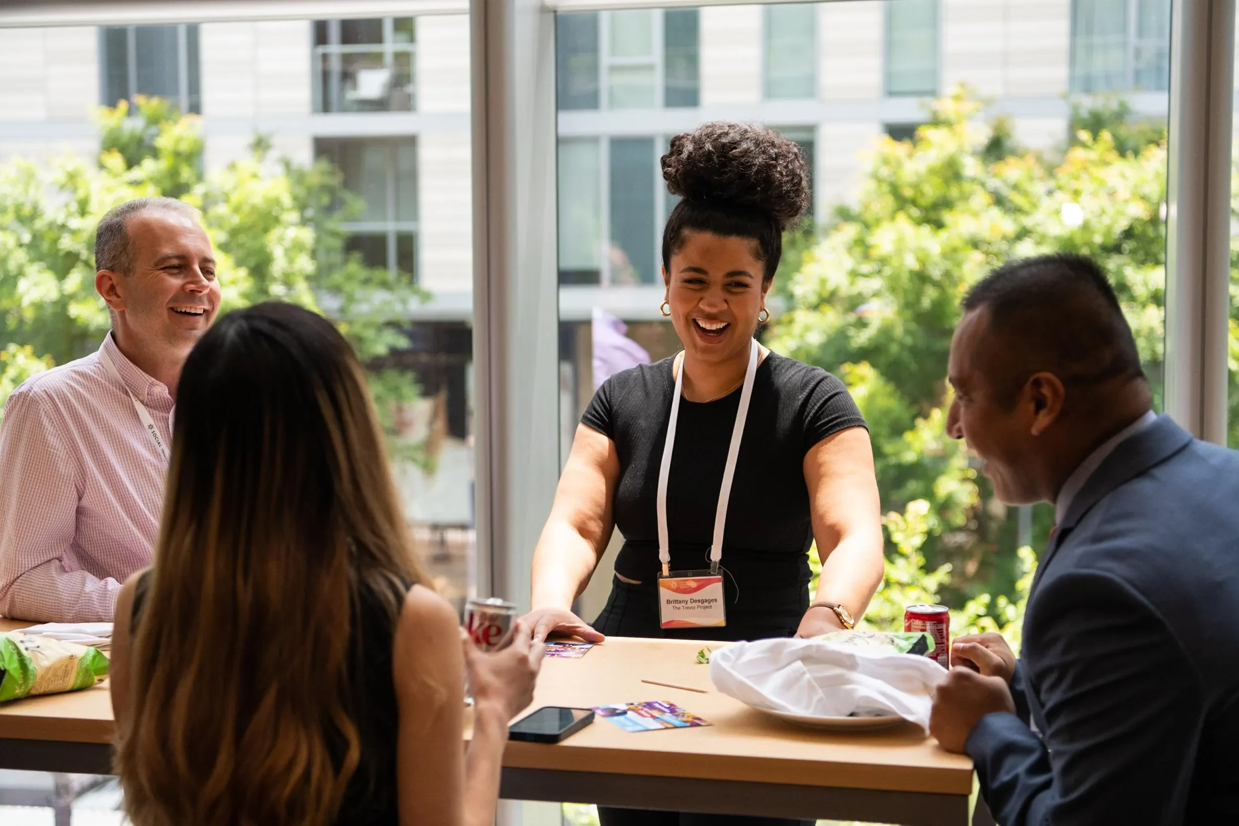 Four people laugh and talk together around a table at a community gathering.