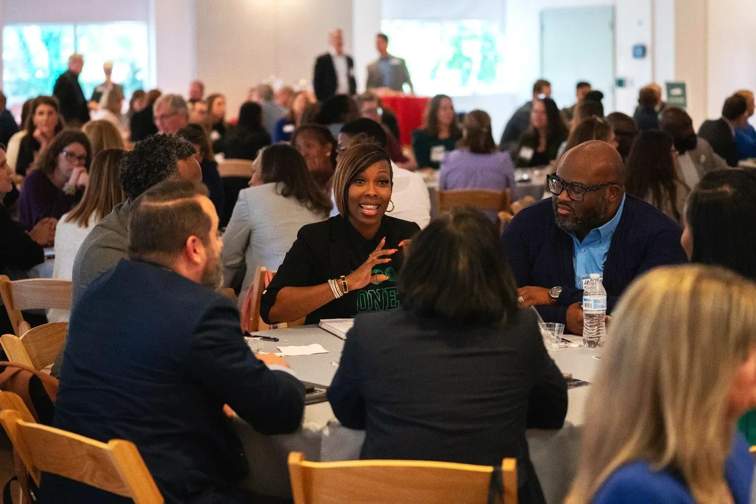 Participants engage in small-group discussions around tables at a large community gathering.