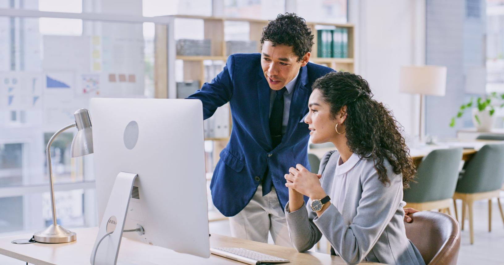 Two professionals reviewing information together on a computer in an office.