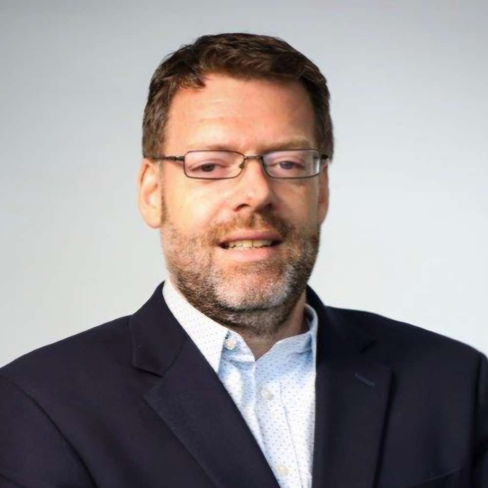 Professional headshot of a man with glasses wearing a navy blazer.