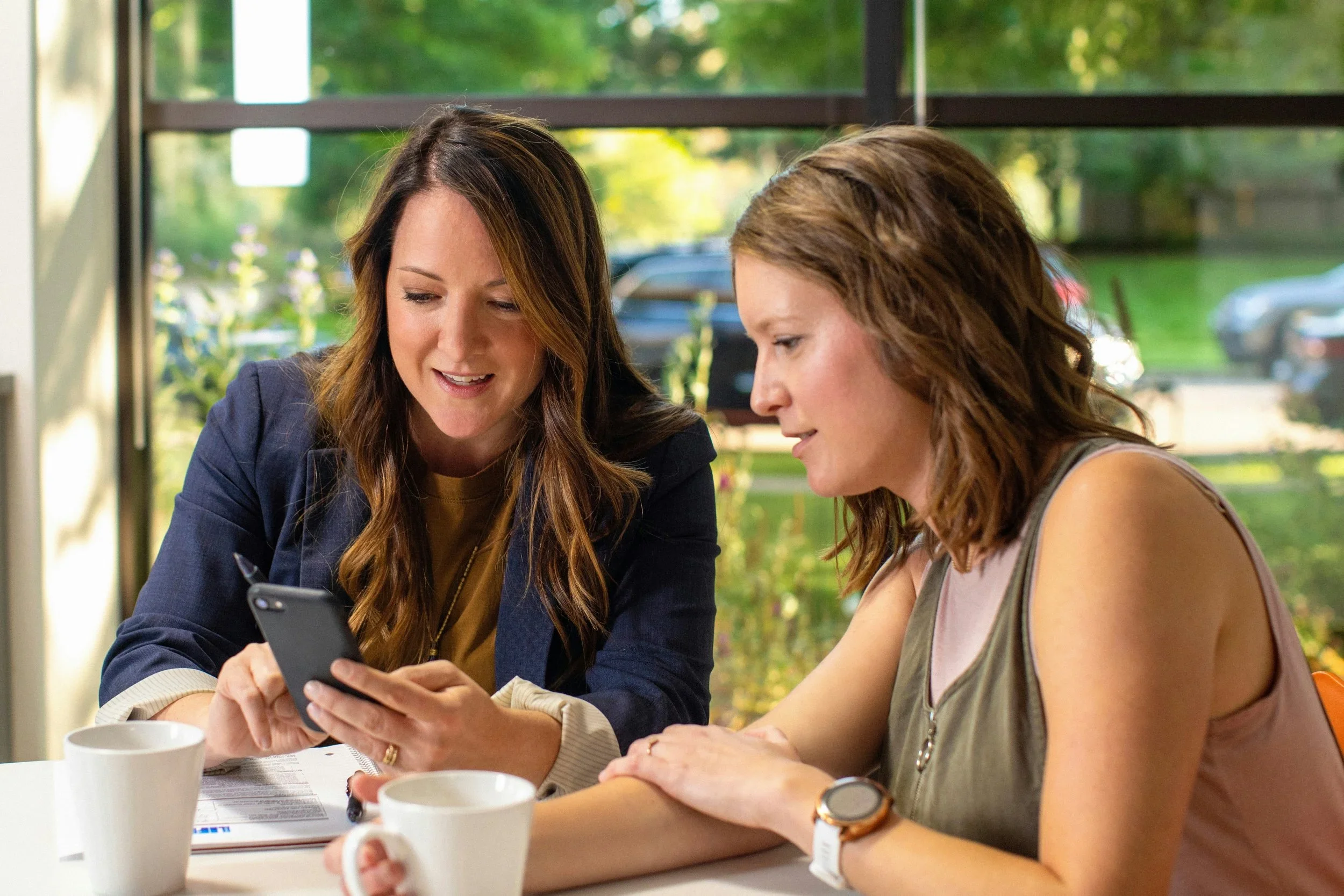 Two women smiling and working together with a mobile device.