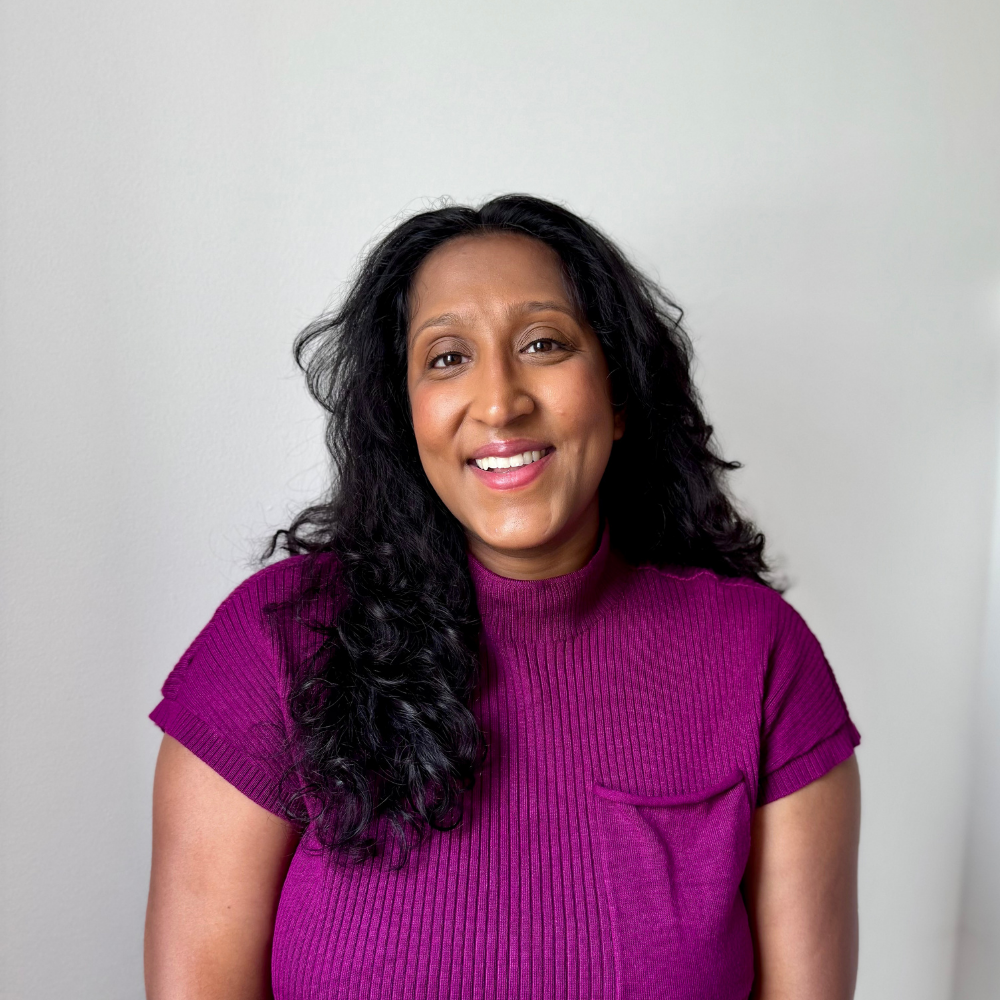 Professional headshot of a smiling woman with long dark hair wearing a purple top.