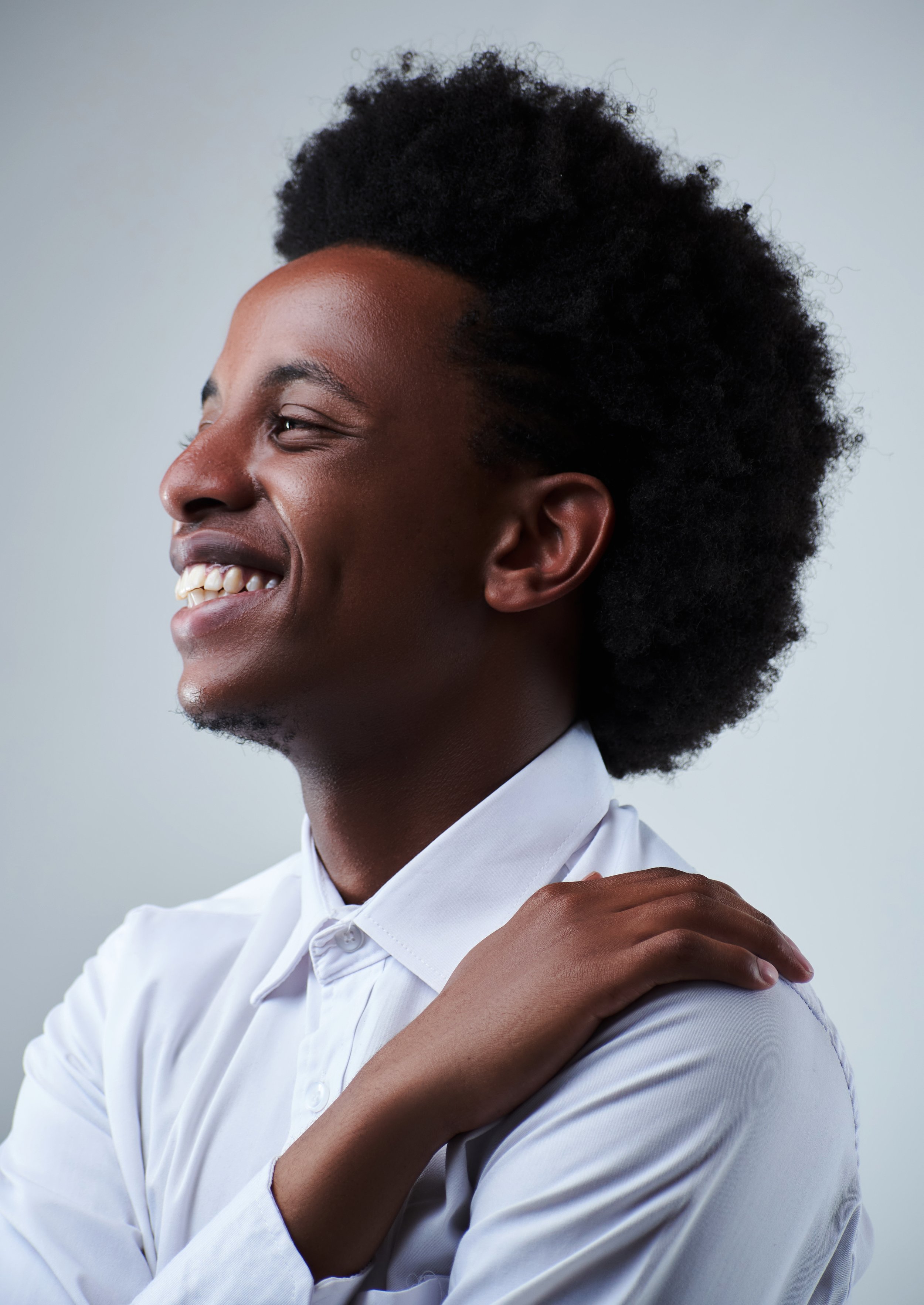 Close-up of an African American woman smiling, wearing a white shirt with a collar, with her hand resting on her shoulder.