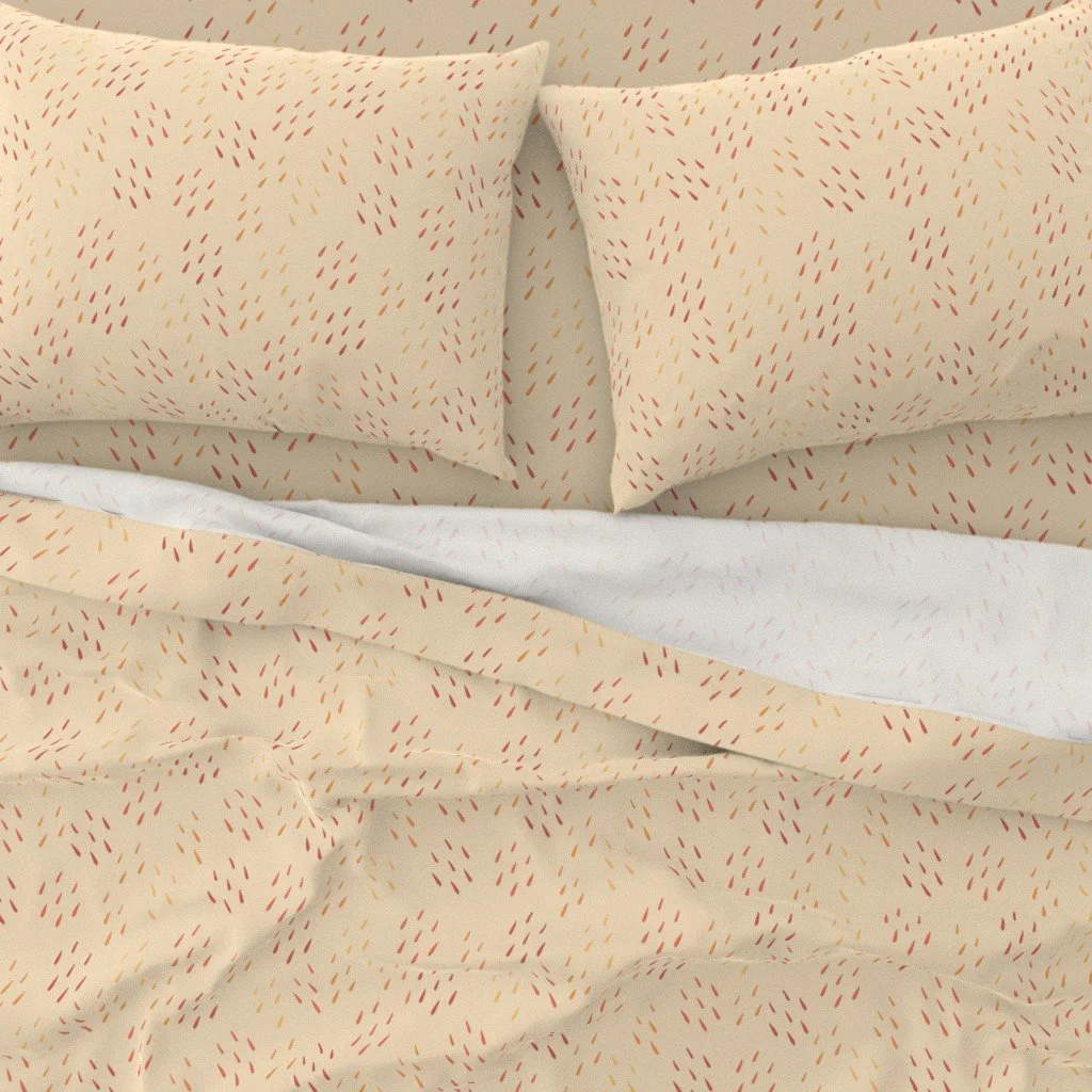 Two beige pillows with red and orange rain drop patterns on a bed with a matching beige duvet with the same pattern.