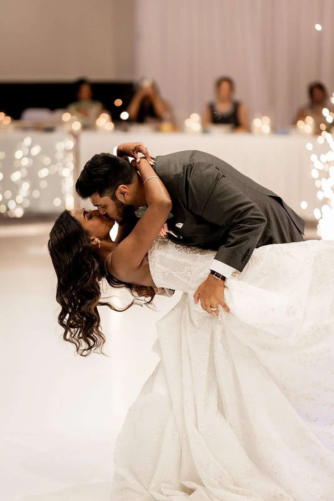 Couple dancing at their wedding, with the groom dipping the bride, who is wearing a white wedding gown, and guests sitting at a decorated reception table in the background at Donato reception centre in Adelaide