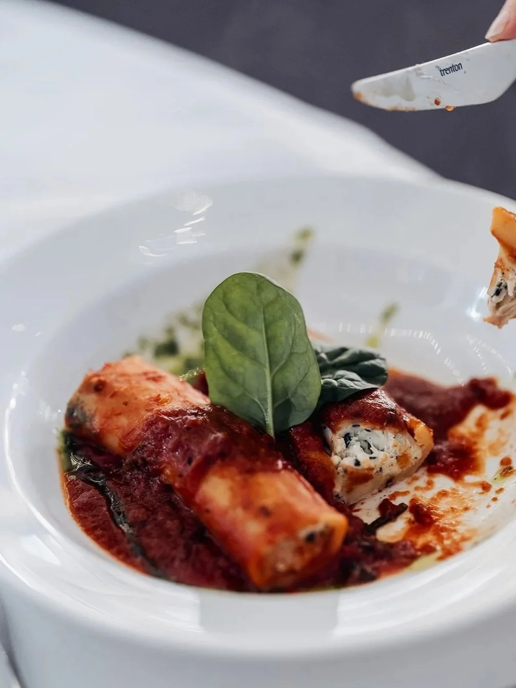 Close-up of stuffed pasta with tomato sauce, garnished with a fresh green leaf on a white plate.