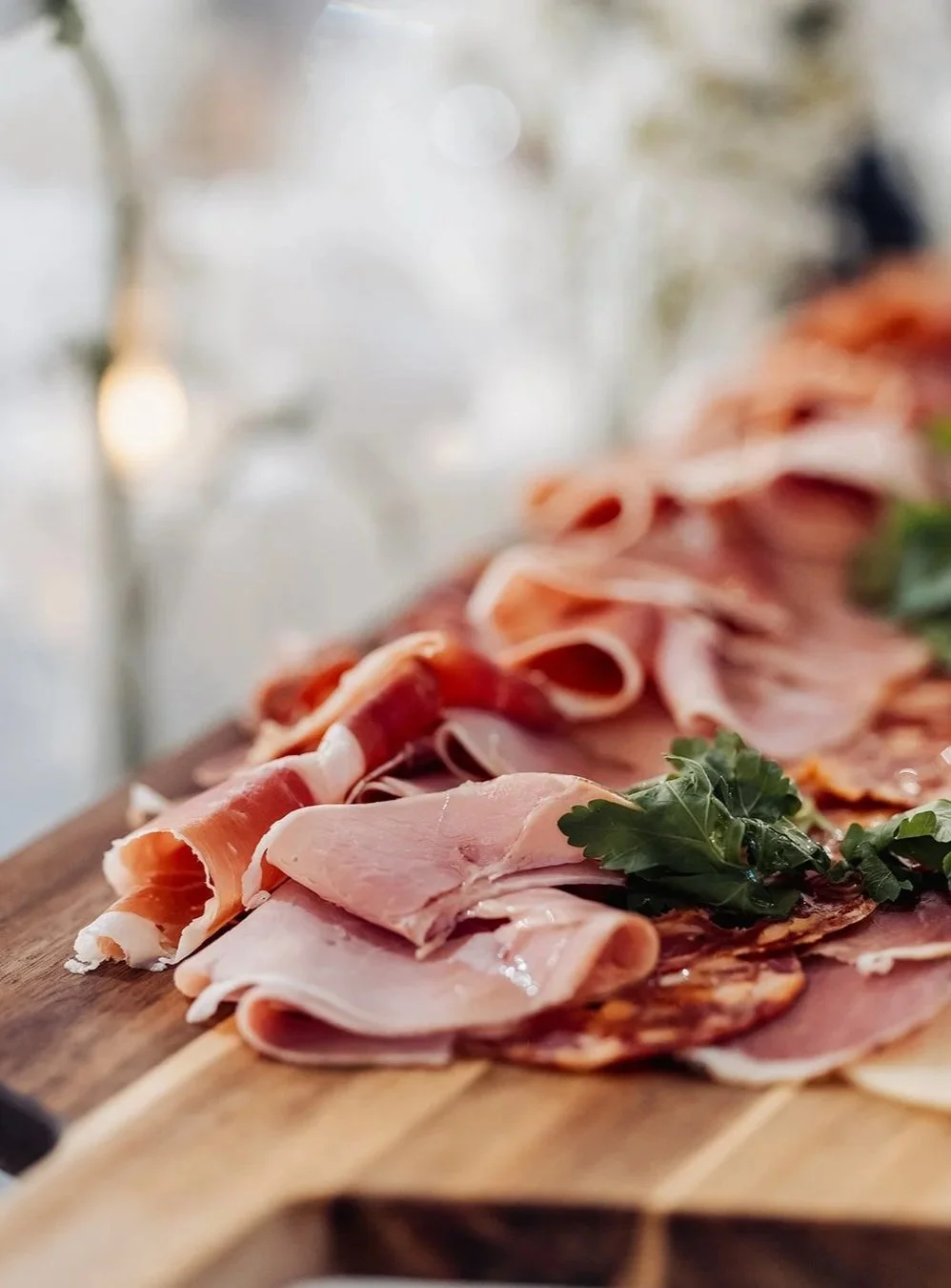 Assorted slices of cured meats on a wooden board with a sprig of parsley.