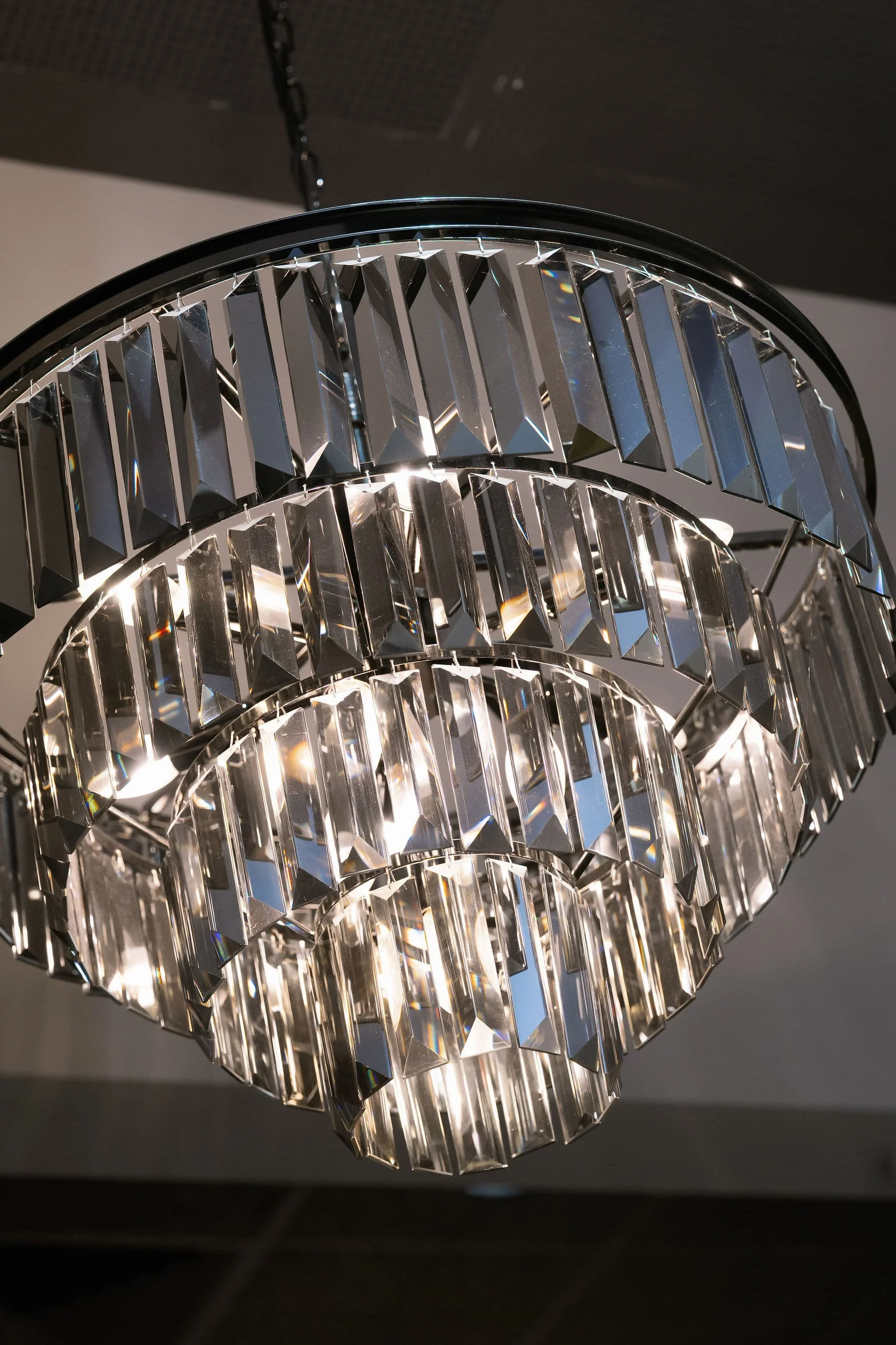 Close-up of a decorative chandelier with multiple geometric cut-glass shapes, hanging from a black chain against a dark background.