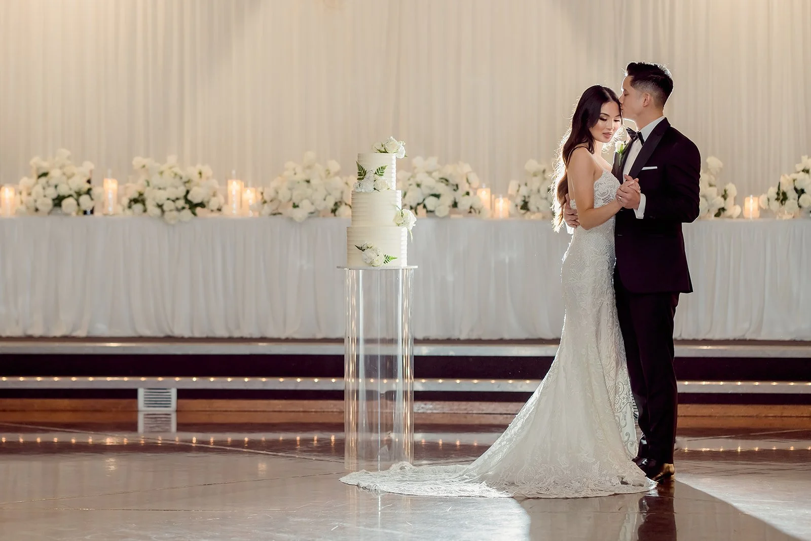 A bride and groom share a dance at their wedding reception, with a decorated table and white floral arrangements in the background at Donato reception centre in Adelaide