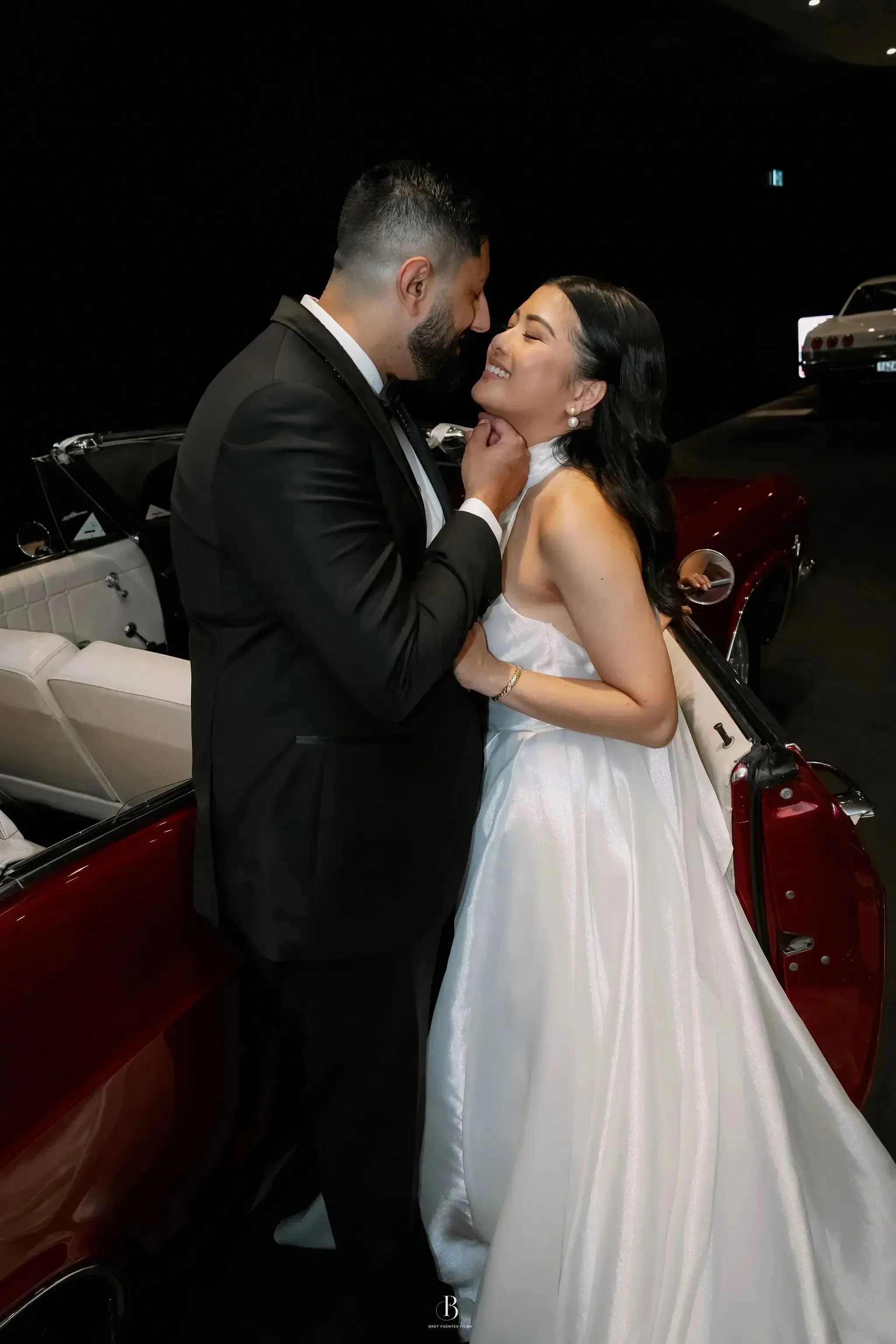The Bride and Groom feeling the love by looking at each other with a nice convertible red car at background.