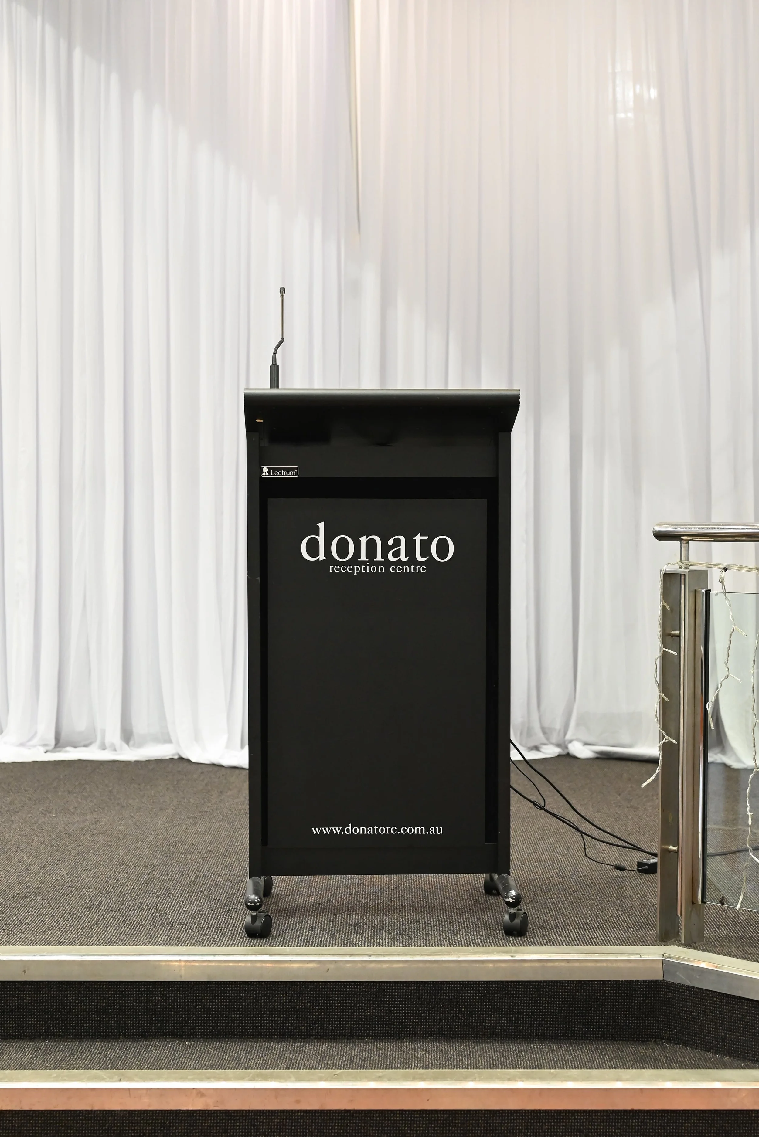 An empty podium with a microphone on a stand in front of a white curtain backdrop at a conference or event venue.