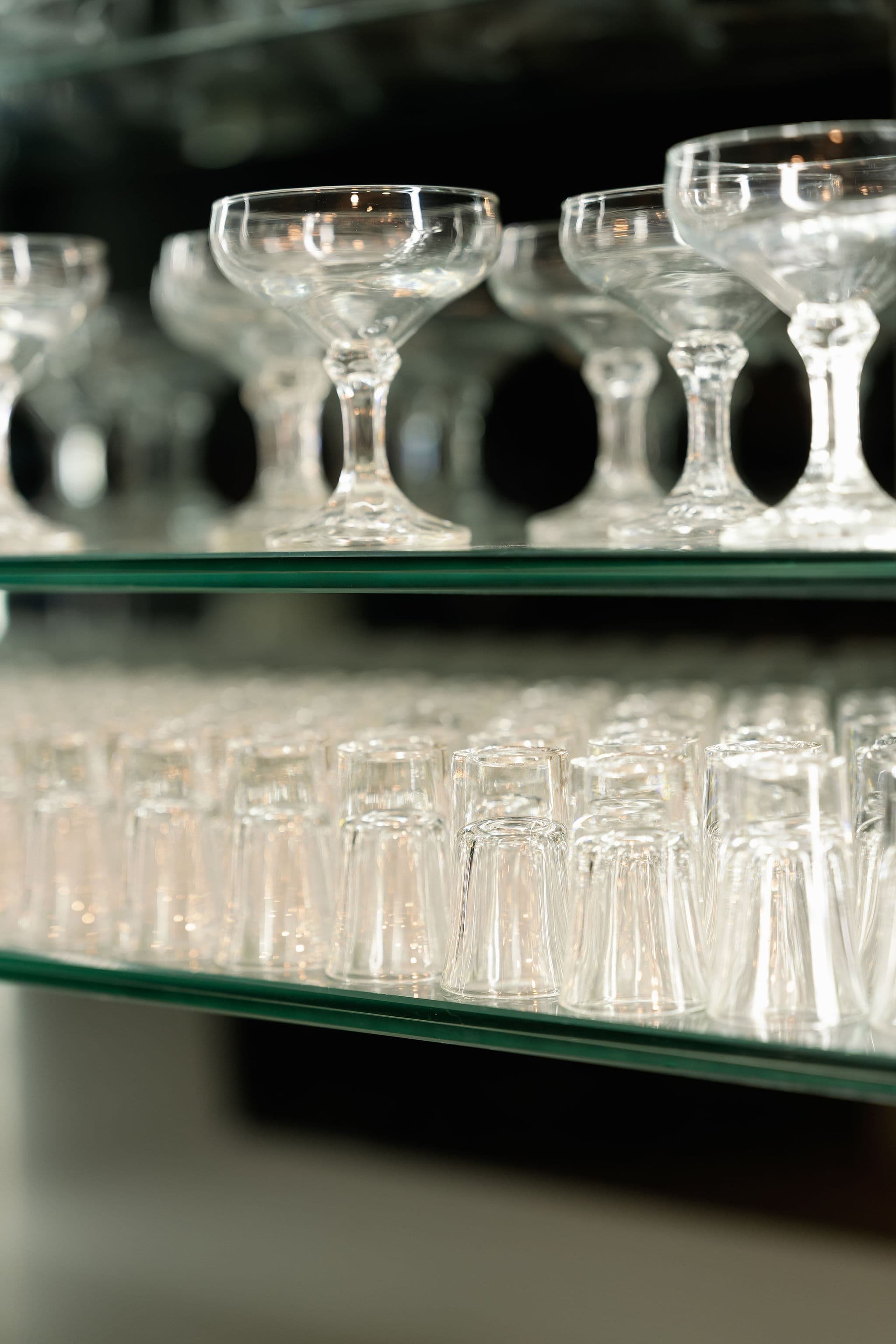 A display of empty glass champagne coupes on glass shelves.